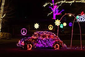 Decorated car surrounded by holiday lights, peace symbols, flowers, and peace signs during nighttime.