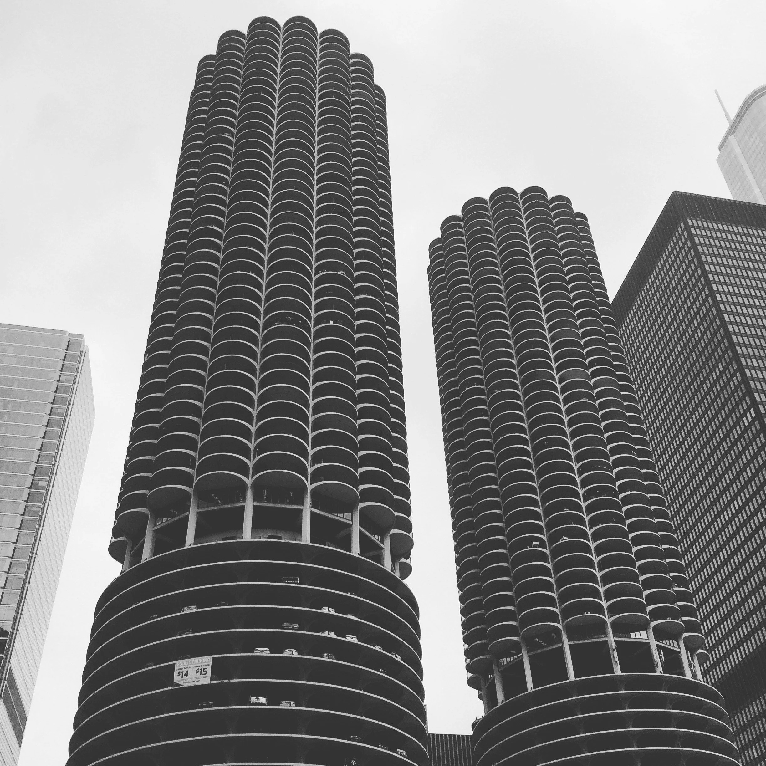 Black and white photo of two modern high-rise buildings with rounded balconies, surrounded by other skyscrapers in an urban cityscape.