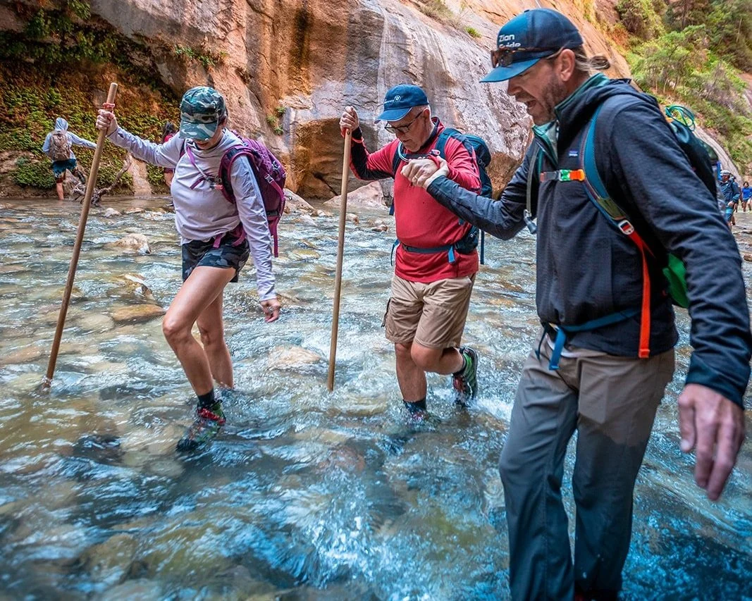 A guide helps two customers wade through water in the Narrows in Zion