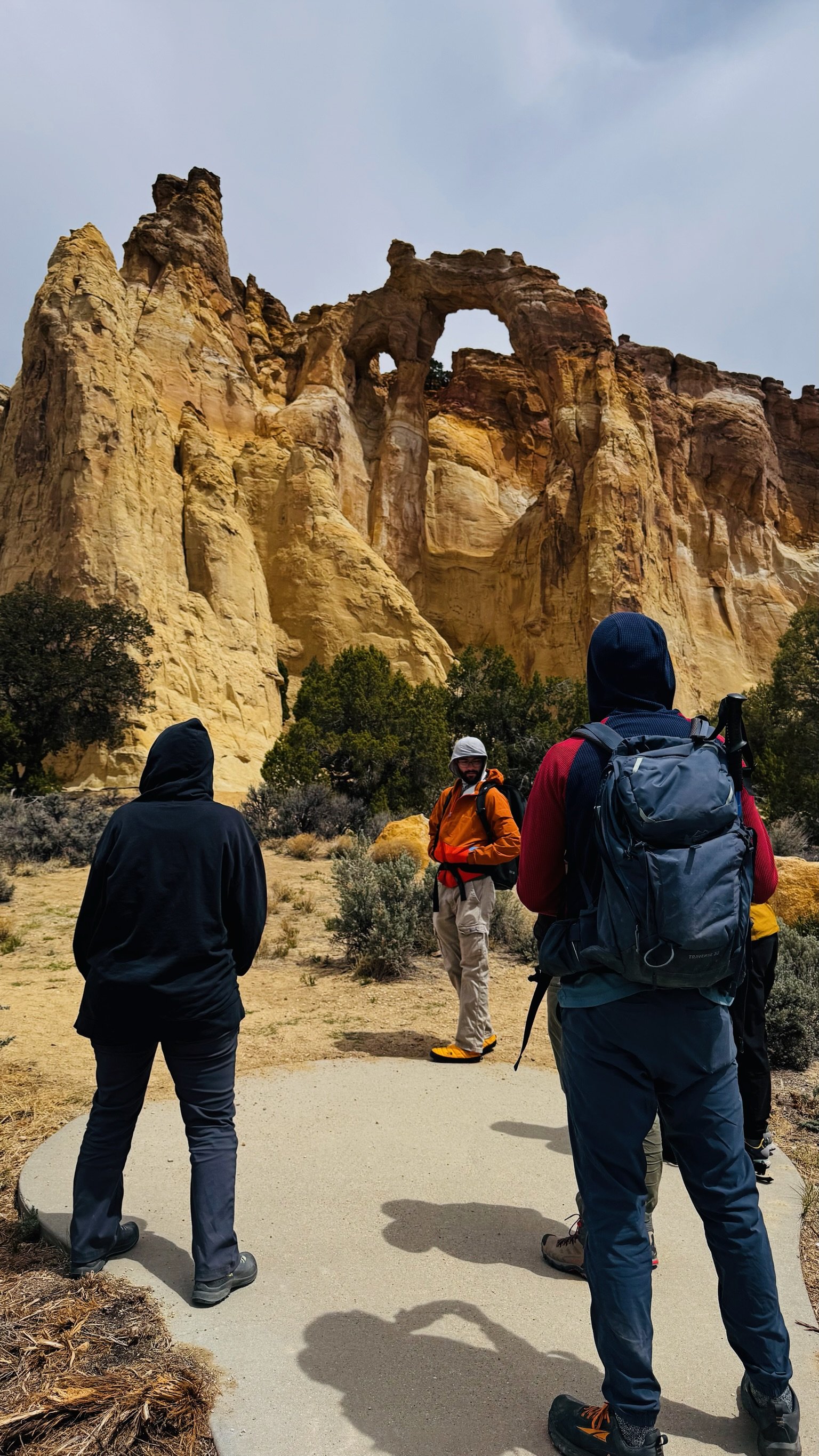 Hikers in a desert landscape with large rock formations and natural arch