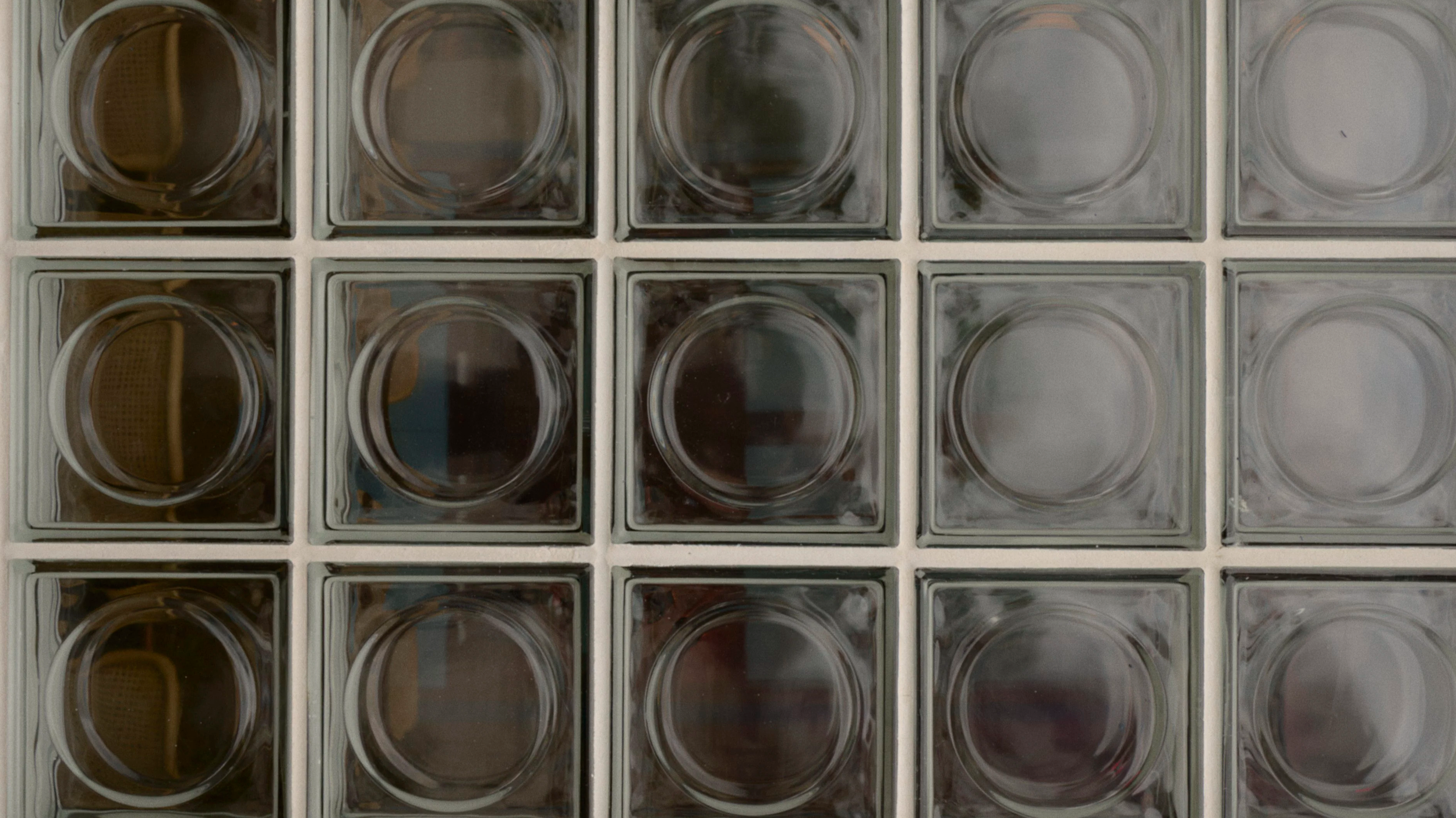 A close-up of a collection of glass blocks arranged in a grid, with some blocks containing circular transparent glass containers inside.