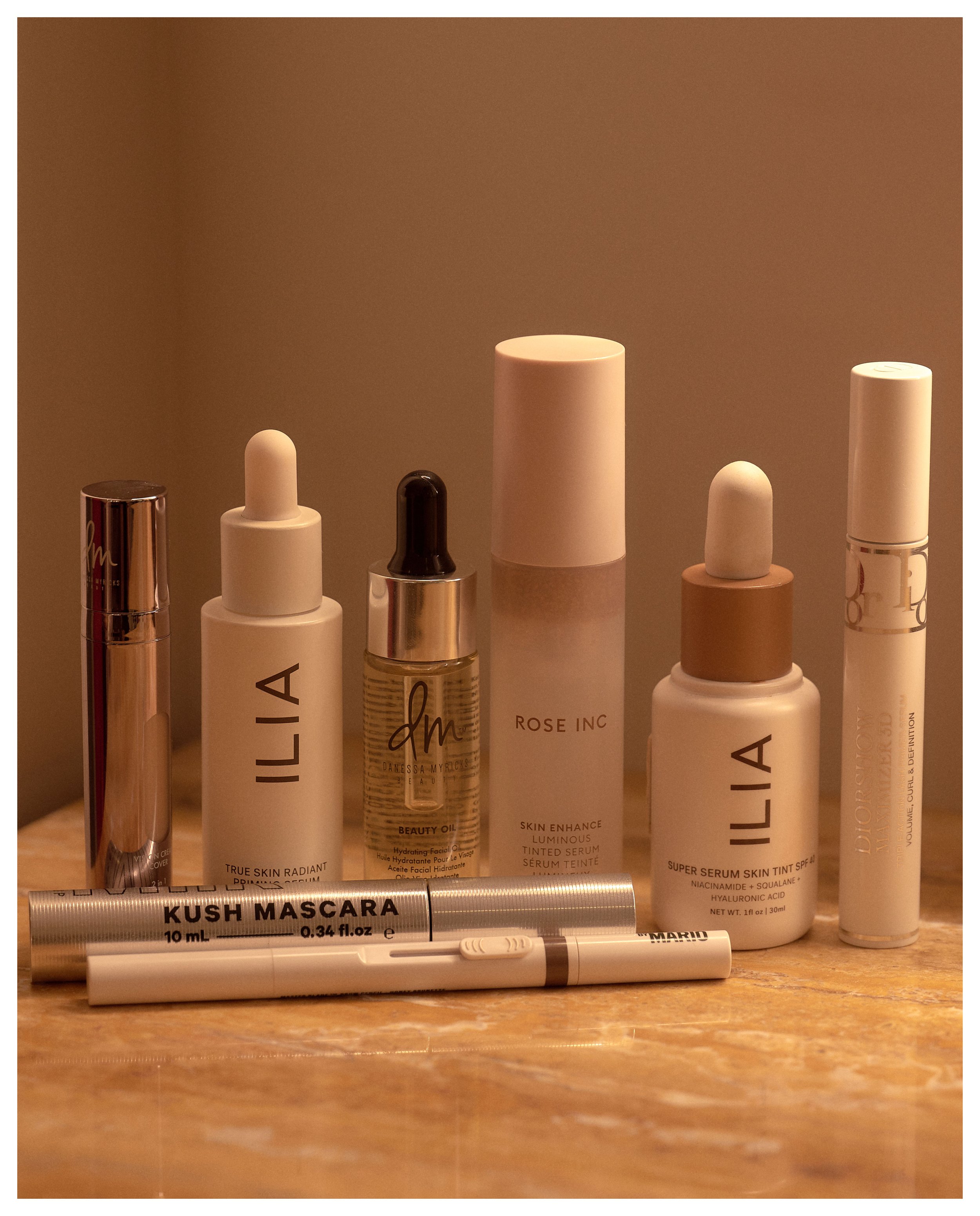 A collection of skincare and beauty products, including bottles and a tube labeled with various skincare brand names and descriptions, arranged on a wooden surface with a beige background.