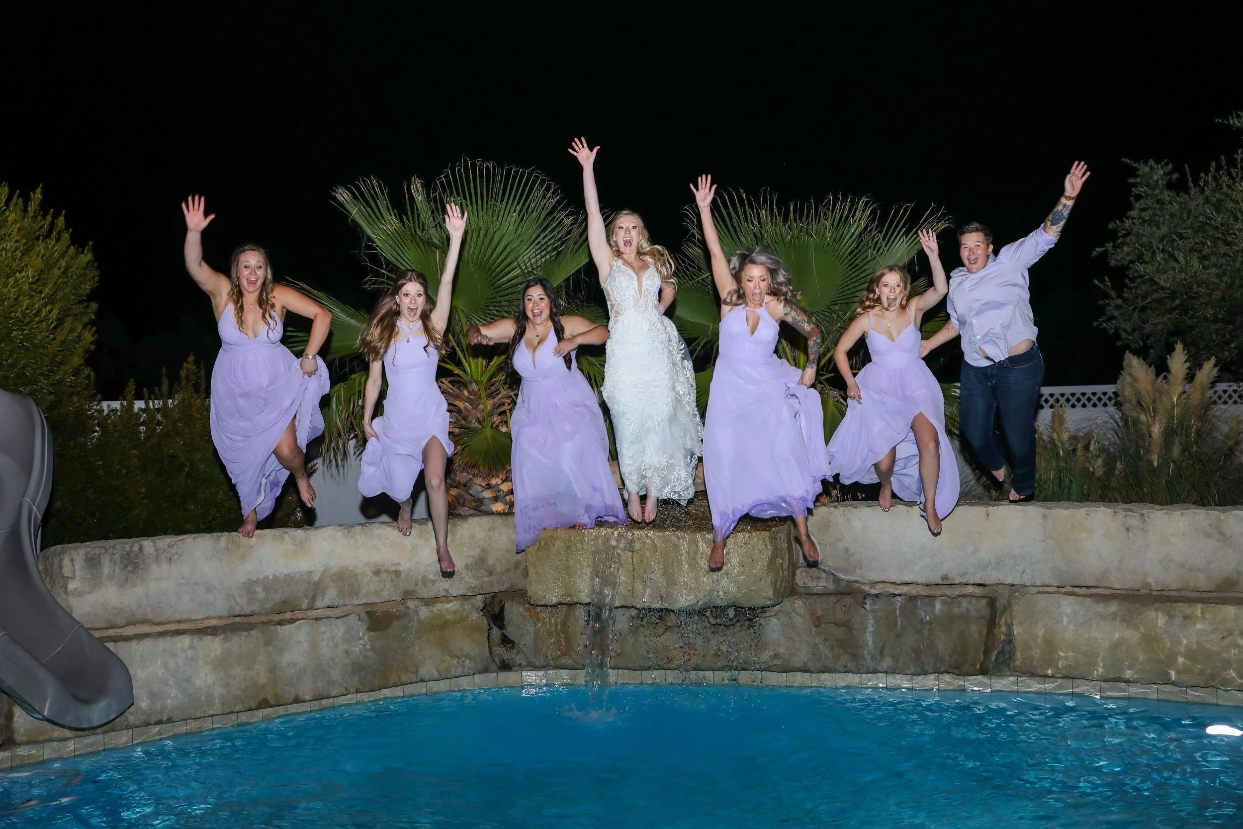 Bride and bridesmaids jump in the pool in wedding dress during reception