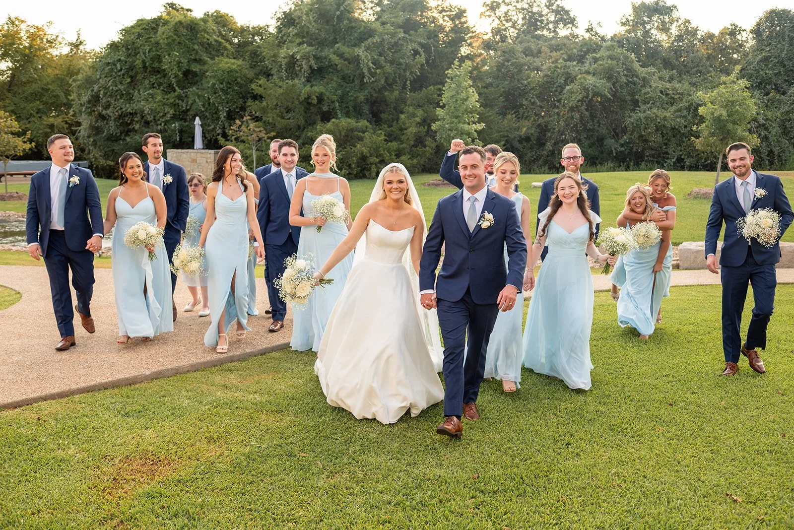 Cameron, Makenzie and their bridal party walking beside the lake at their Bryan, Texas wedding venue.