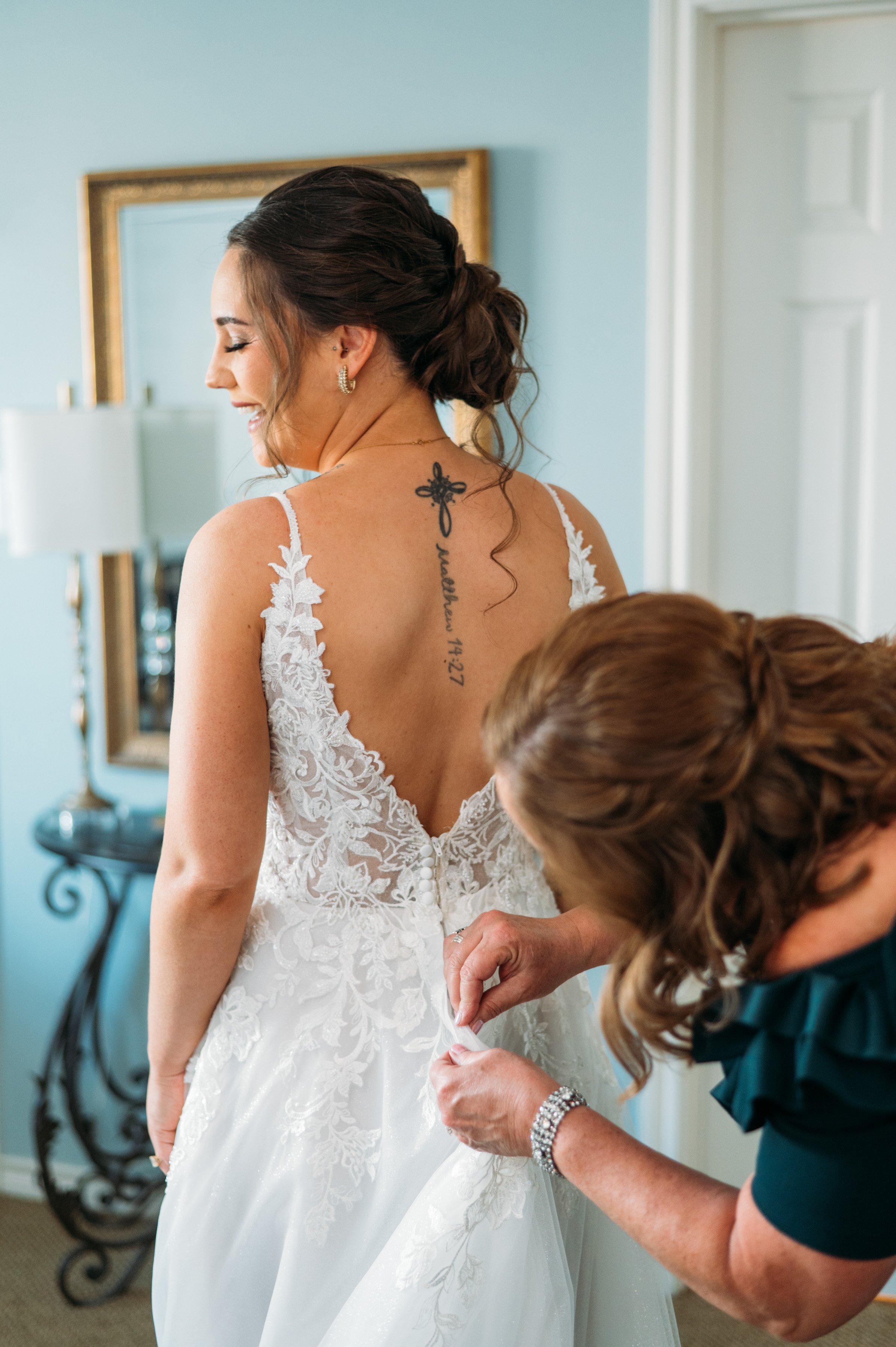 Mother of the bride helps bride button up her dress in the bridal suite at Inn at Quarry Ridge