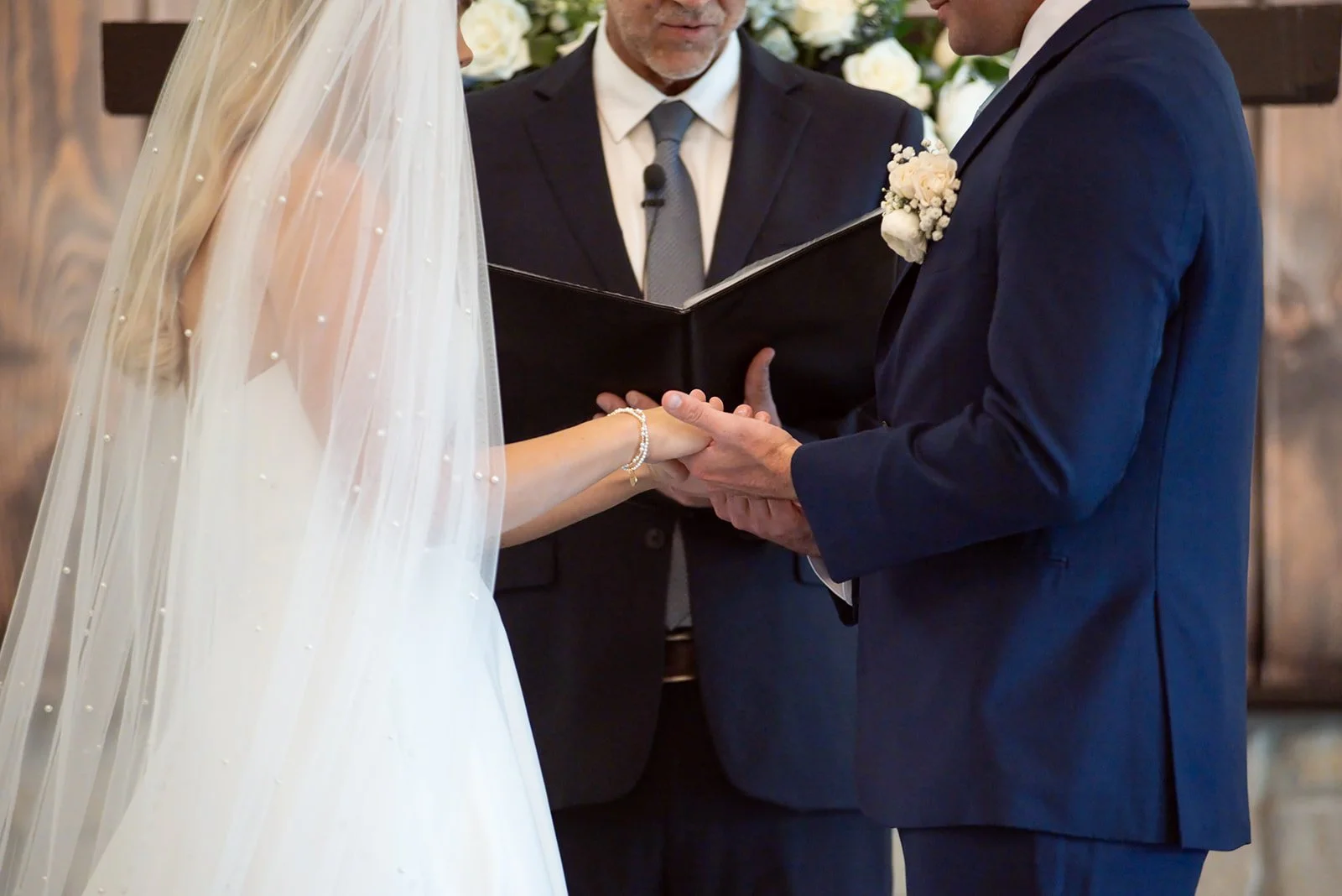 Bride and groom holding hands at the altar during their indoor wedding ceremony.
