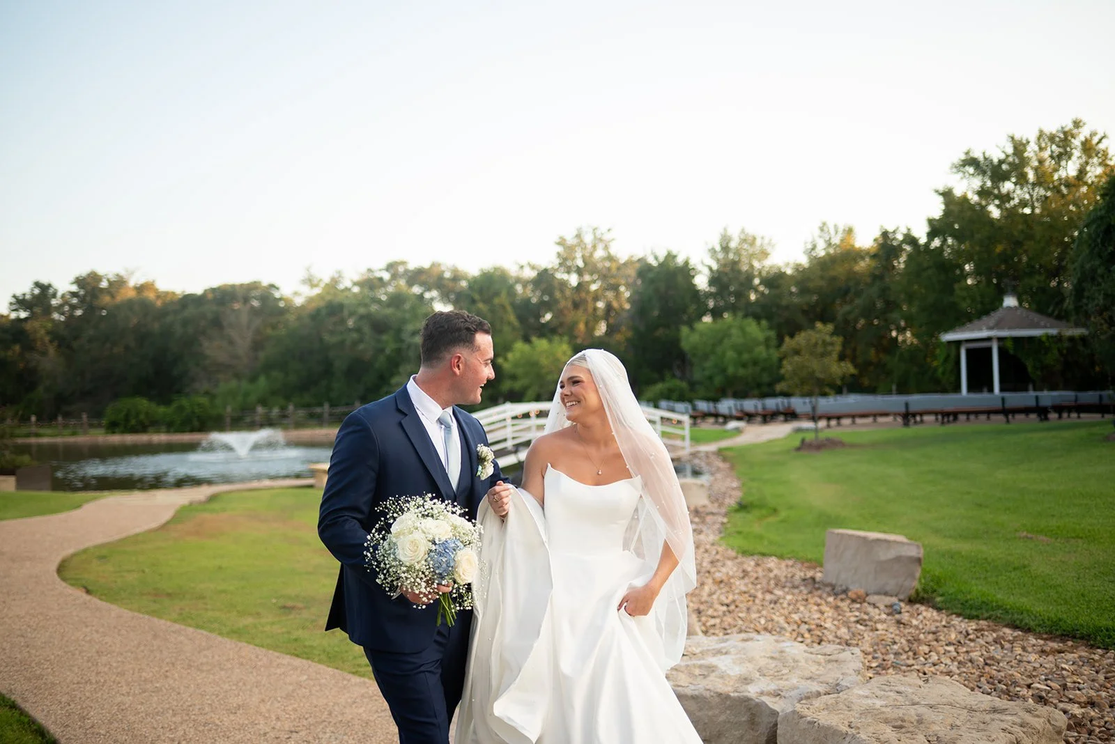 Cameron and Makenzie walking hand in hand beside the lake at their wedding venue in College Station Tx