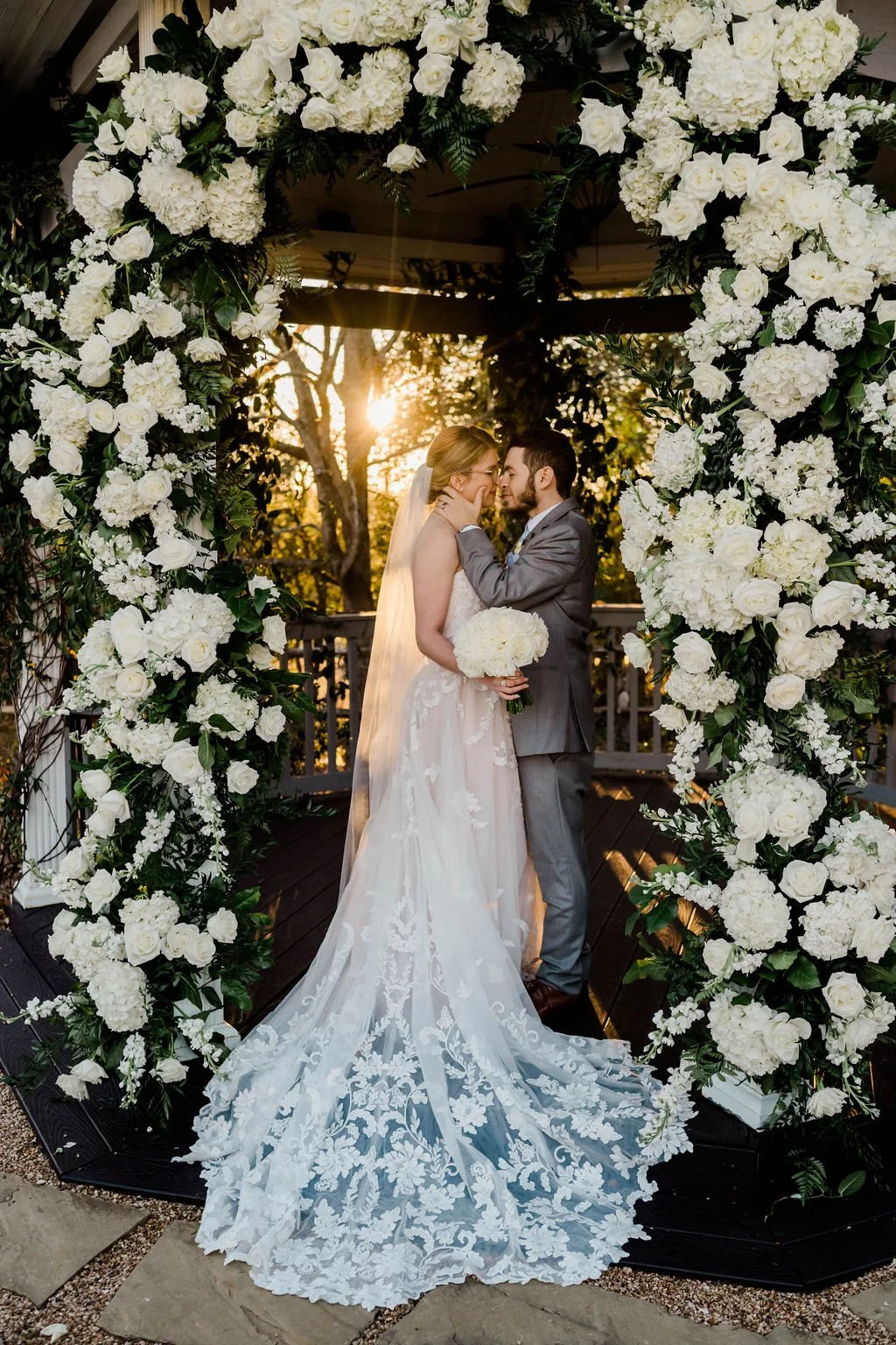 Bride and groom share a kiss under outdoor ceremony gazebo surrounded by flowers