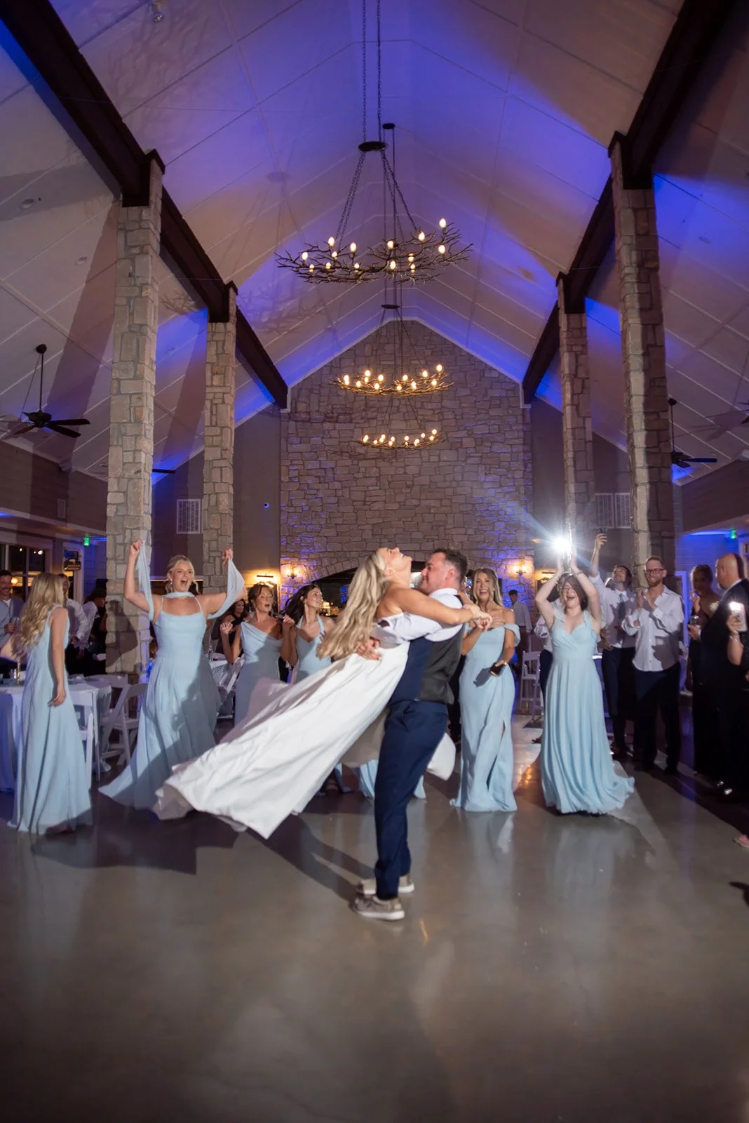 Groom twirls his bride around with wedding guests celebrate at reception.