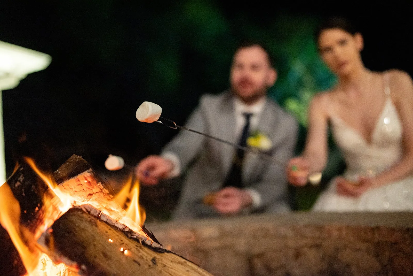 Bride and groom roast marshmallows at the fire pit during wedding weekend
