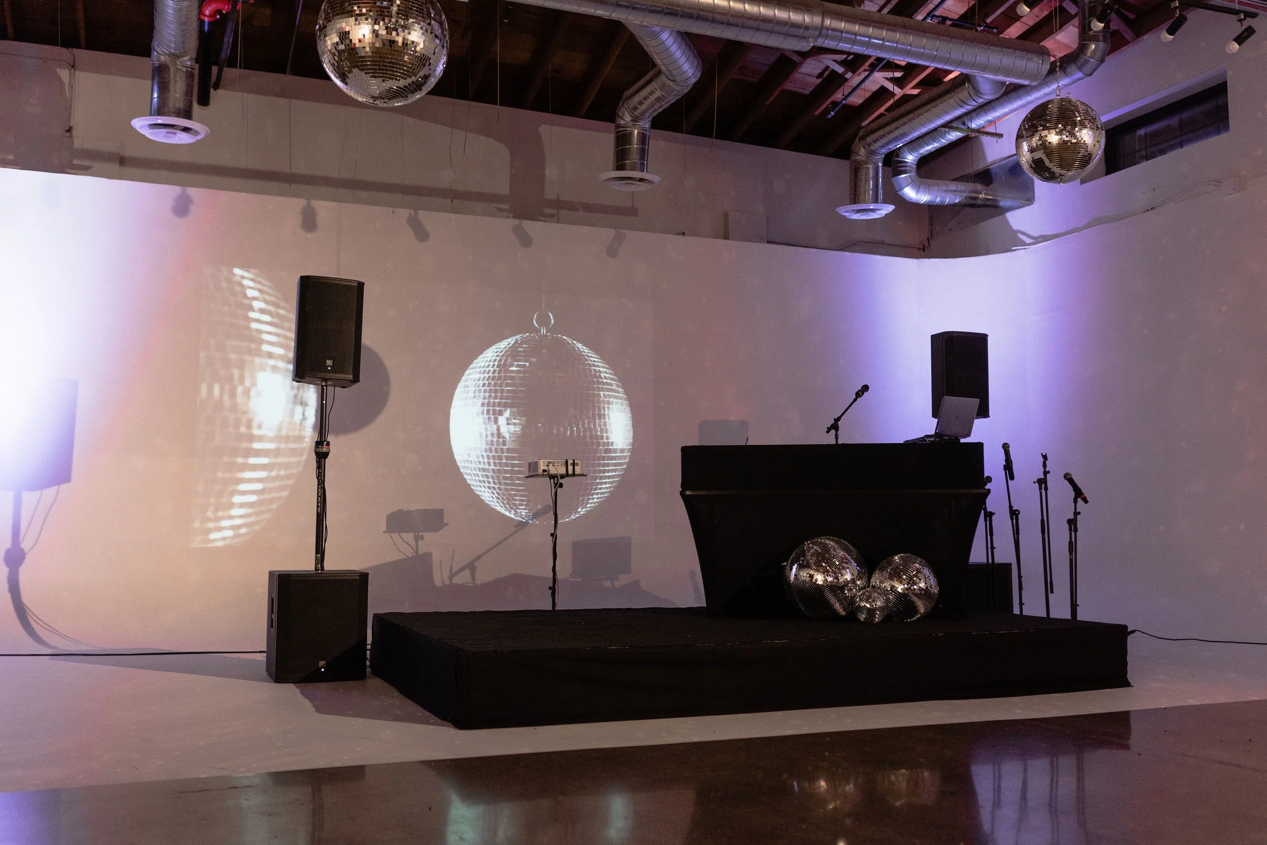 Empty event space or gallery with industrial-style ceiling pipes, polished wooden floor, and large white display walls.