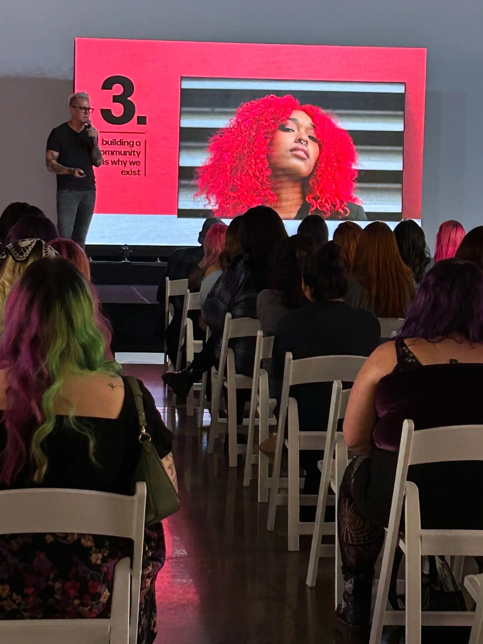 People socializing at an indoor event with disco balls hanging from the ceiling and a large projected 'YET.' on the wall in pink and orange lighting.