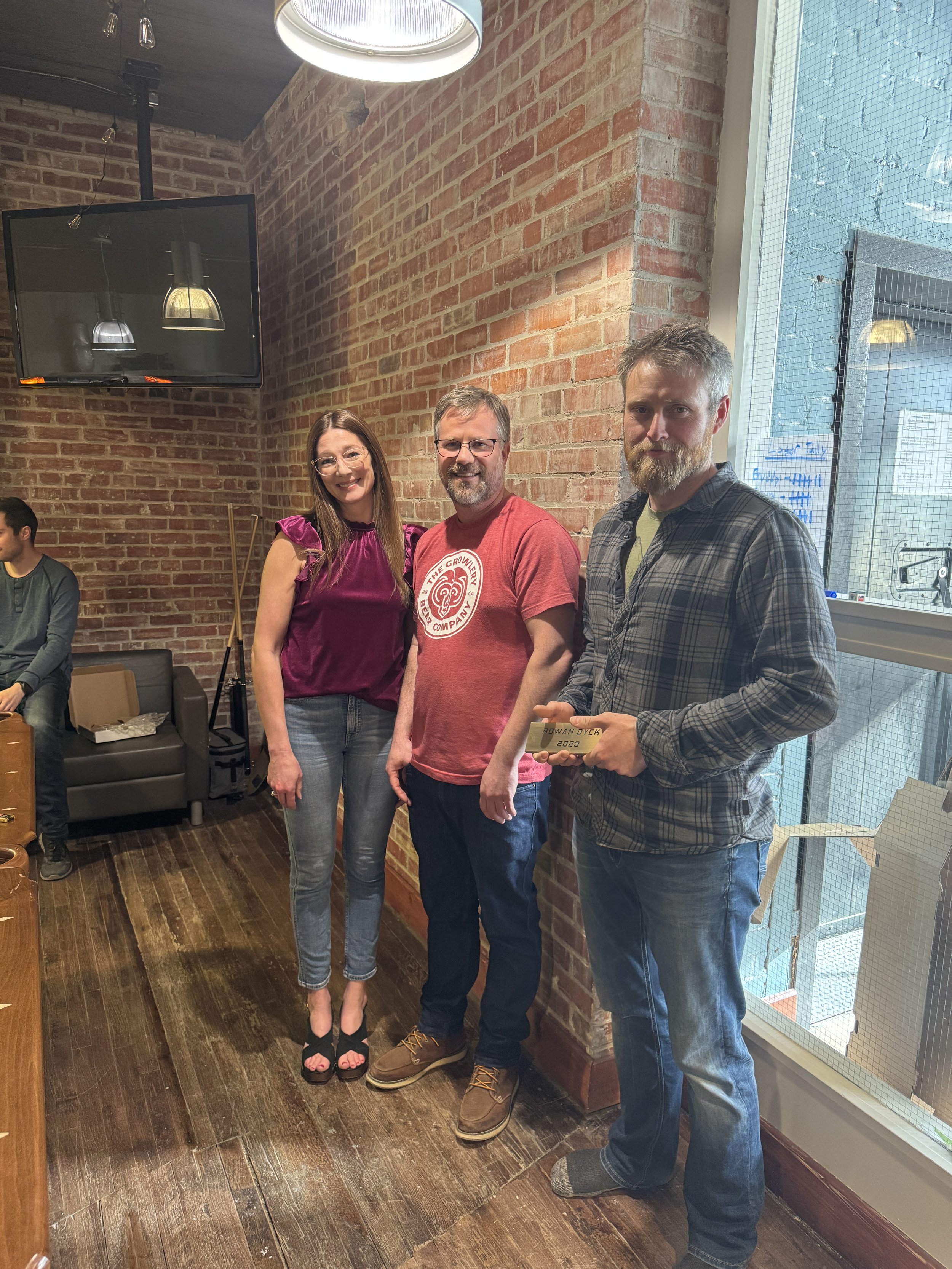 Three people dressed in regular attire at an indoor event, standing in front of a window.