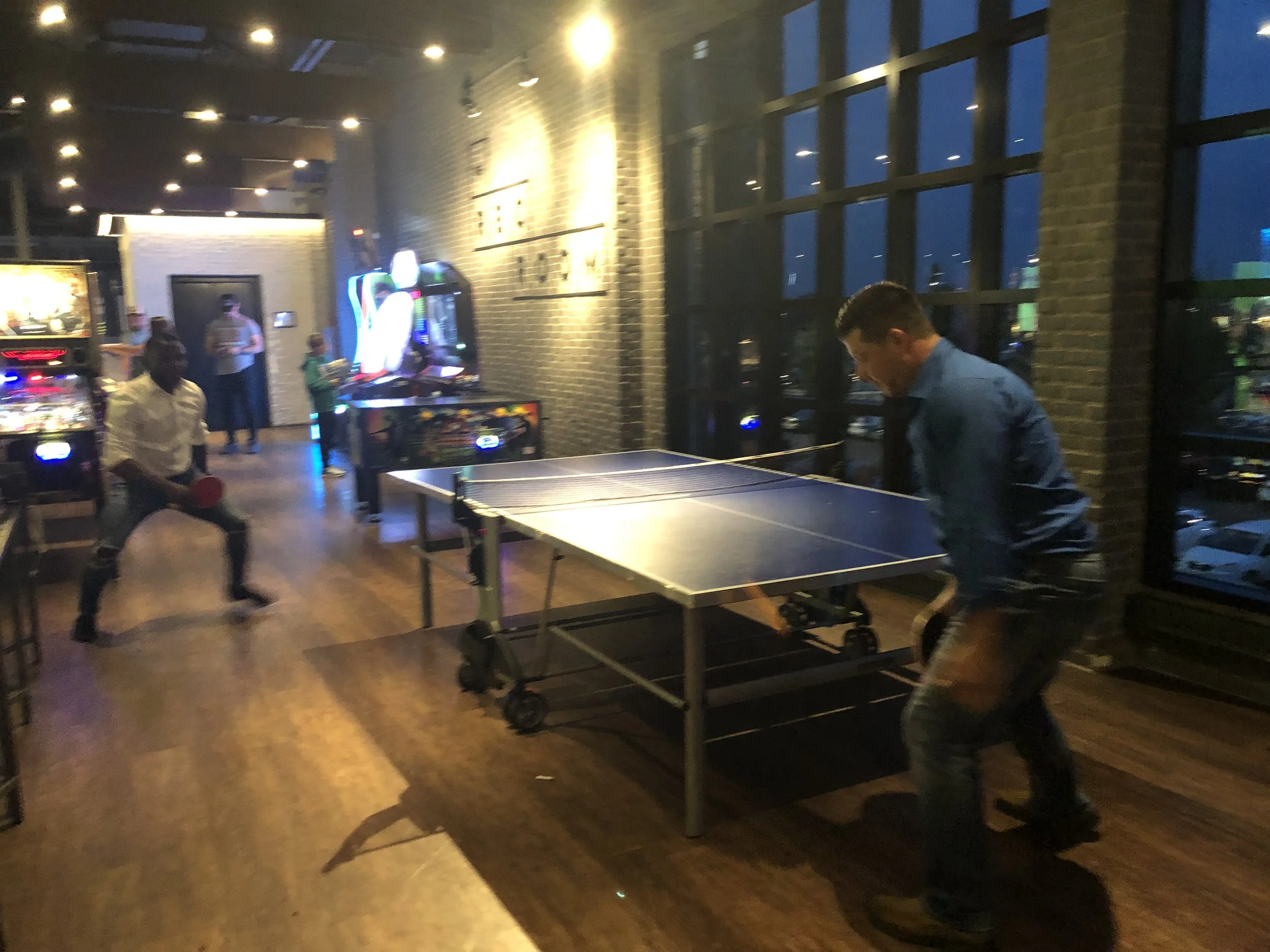 Two people playing table tennis in an arcade with pinball machines.