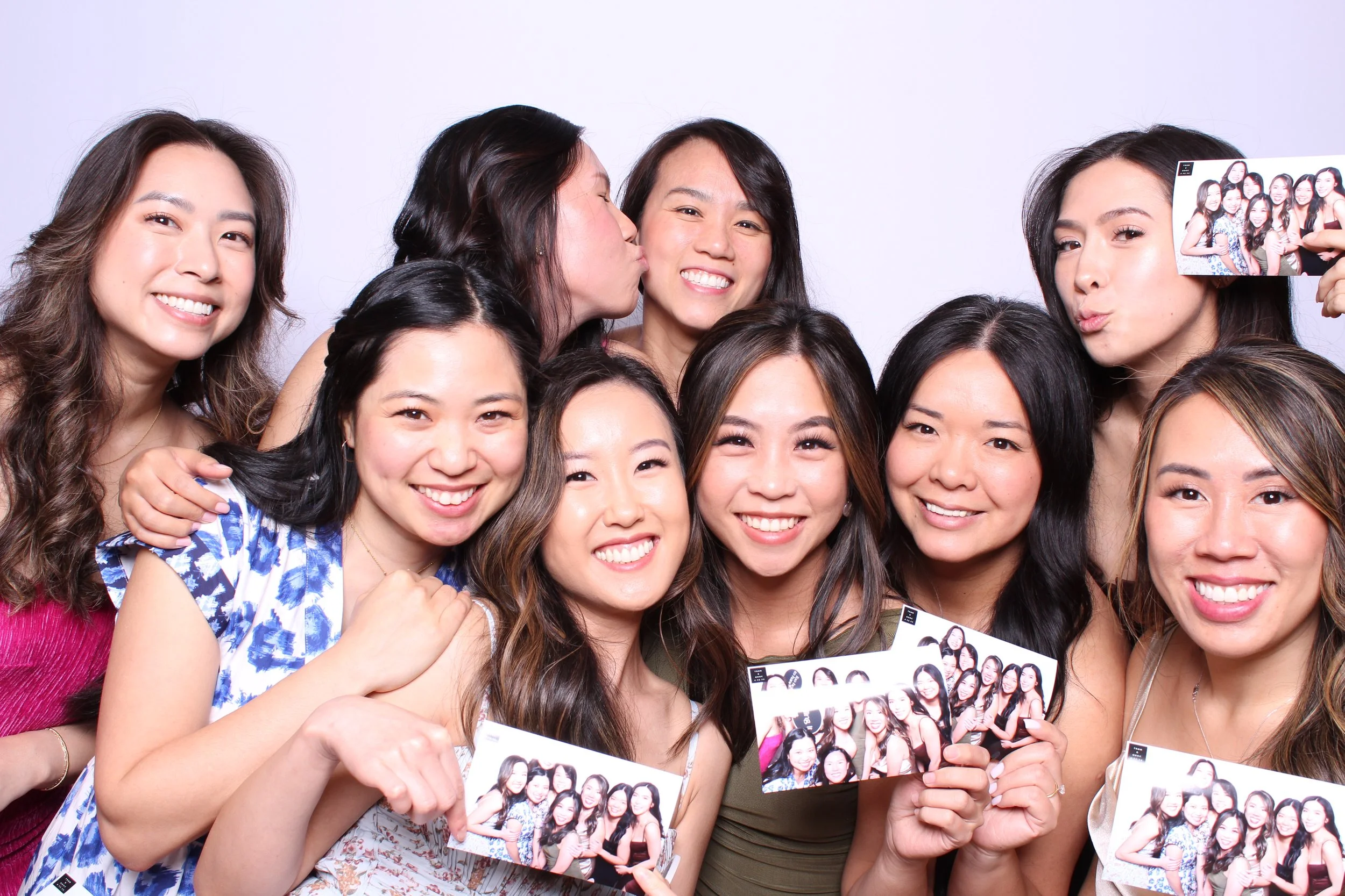 A group of female wedding guests smiling and holding their 4x6 photo booth pictures