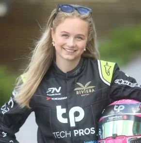 Lilo Fyrileiv smiling, wearing a racing suit and sunglasses on her head, holding a racing helmet.