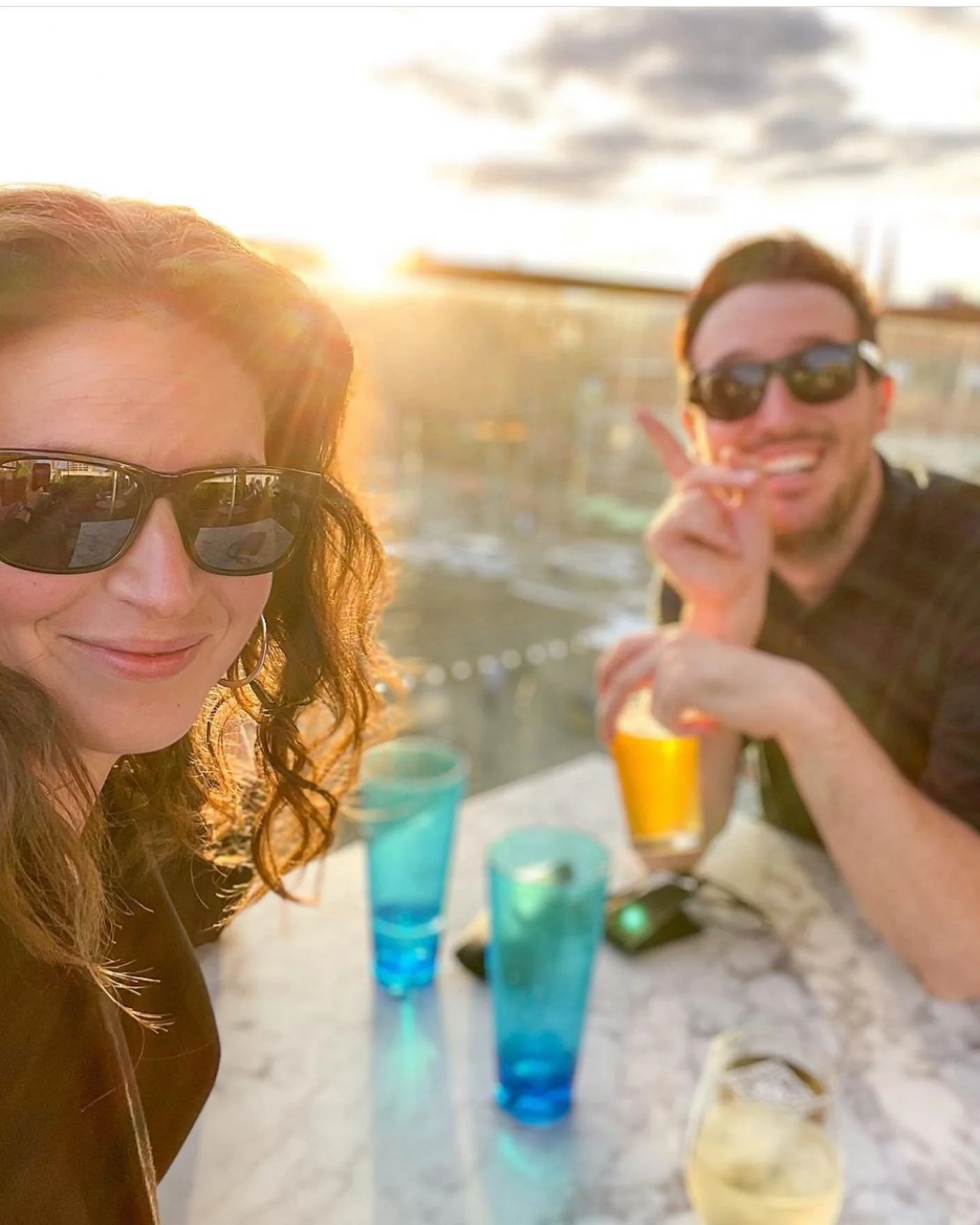 A woman and a man smiling and wearing sunglasses, enjoying a sunset at ByWard market rooftop. copper sights of the sun setting, cocktails, views and the best venue in Ottawa for gatherings and private events 
