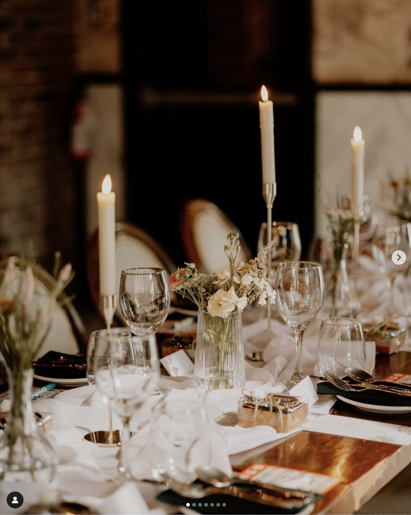 A formal dining table decorated with lit candles, floral centerpieces, wine glasses, plates, and cutlery, set for a special event or celebration.