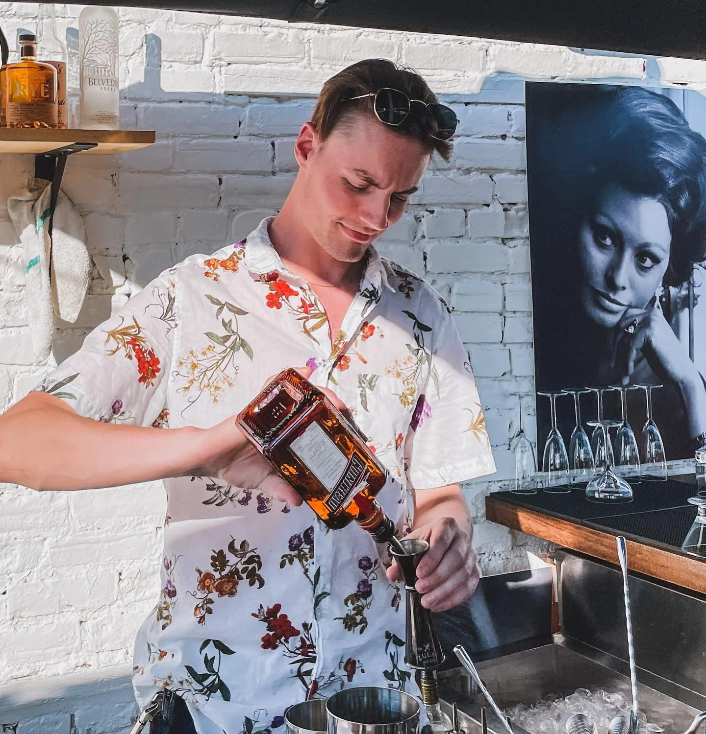 A man in a floral shirt pouring whiskey into a cocktail shaker at a bar. roof top views, our built in bar in the heart of the byWord market. Best Views in town 