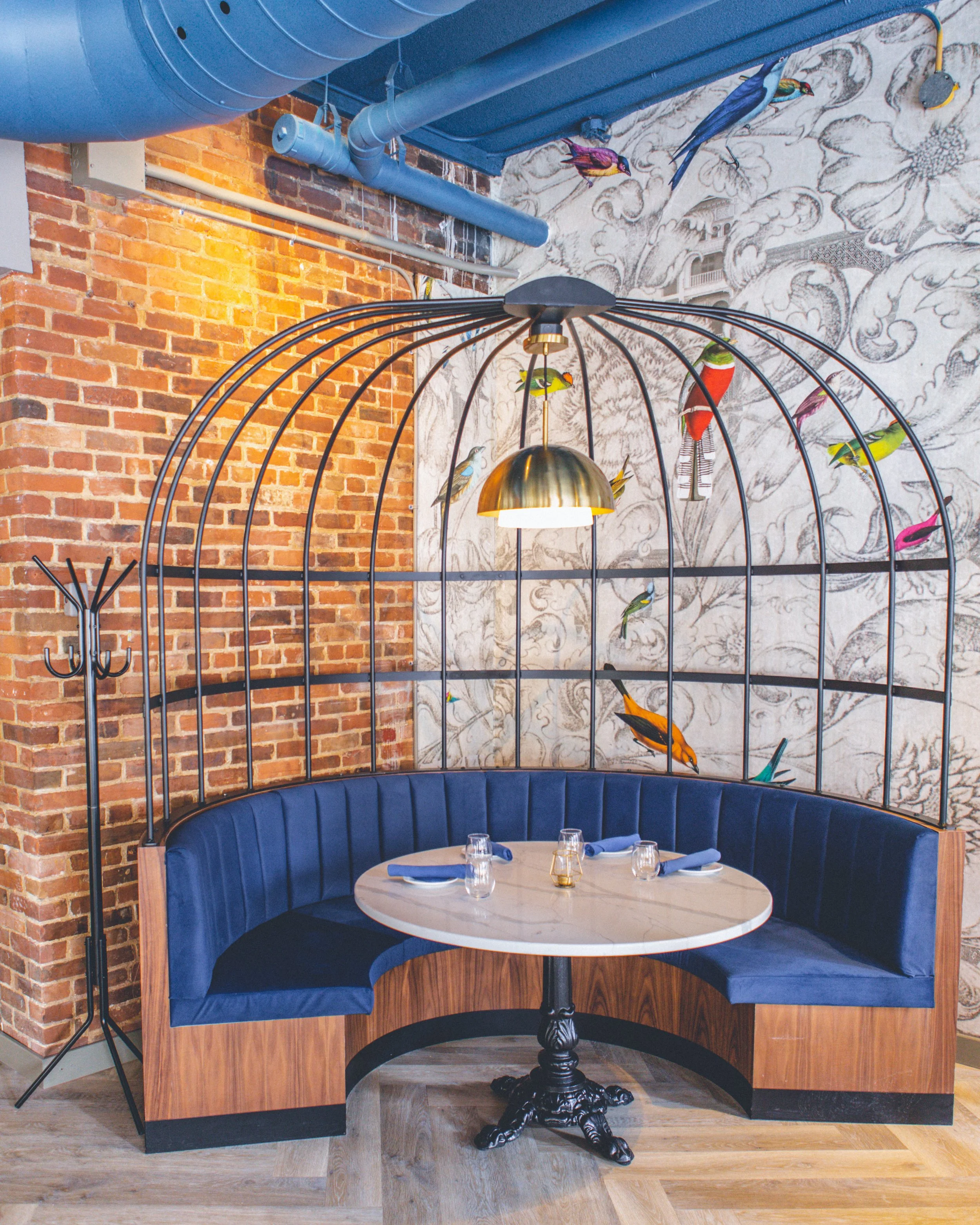 Interior of starling, a modern restaurant in a heritage building. Velvet upholstered booths, with  exposed brick wall, a mural with birds, and a decorative birdcage-like structure hanging from the ceiling a unique venue in Ottawa for private events