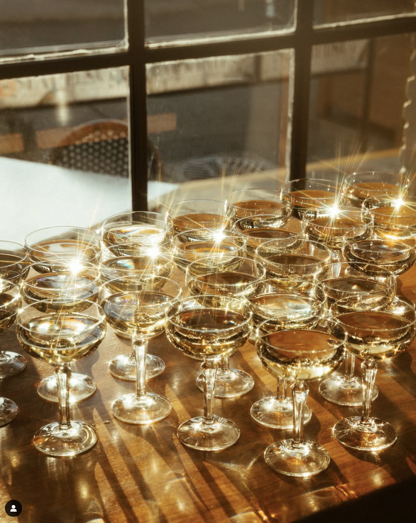 Several glasses of white wine arranged on a table with sunlight reflecting off their surfaces, casting sparkles and shadows.