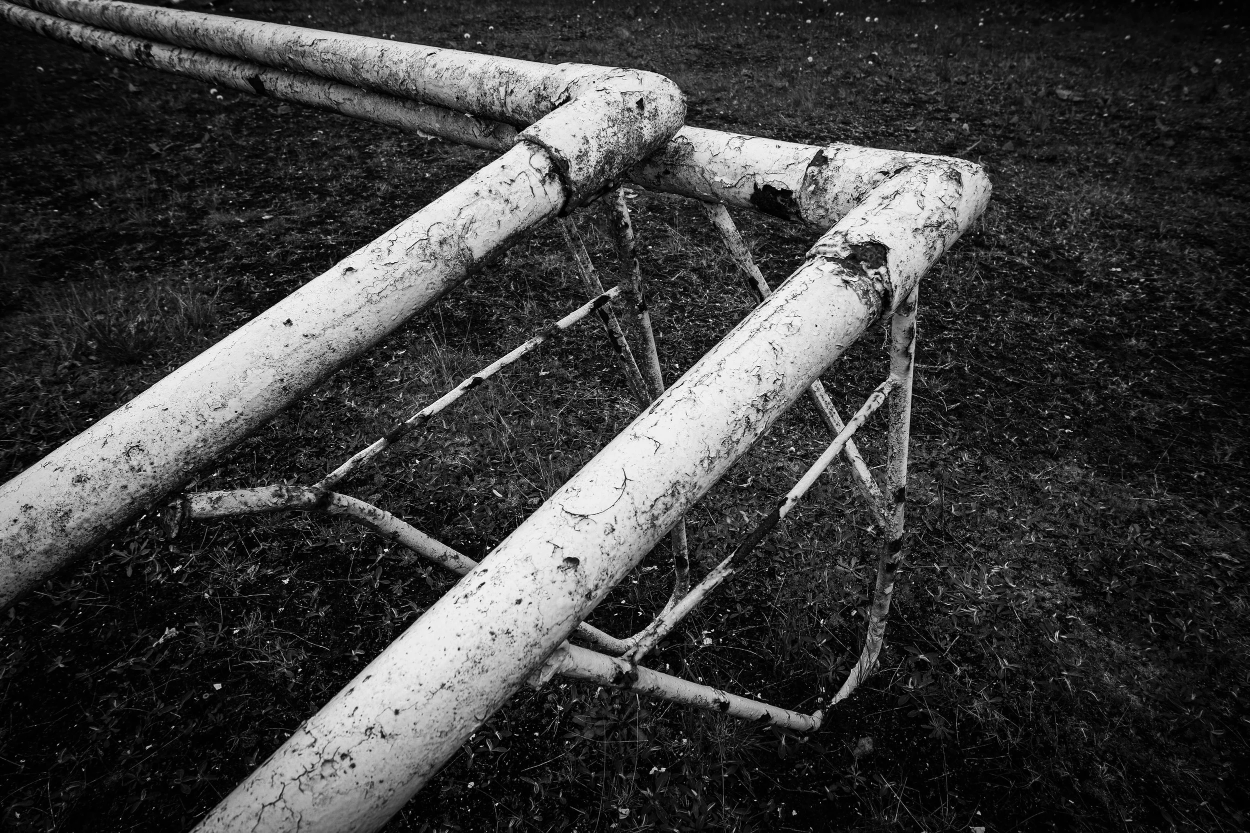 An old, weathered, rusted metal playground structure on grass.