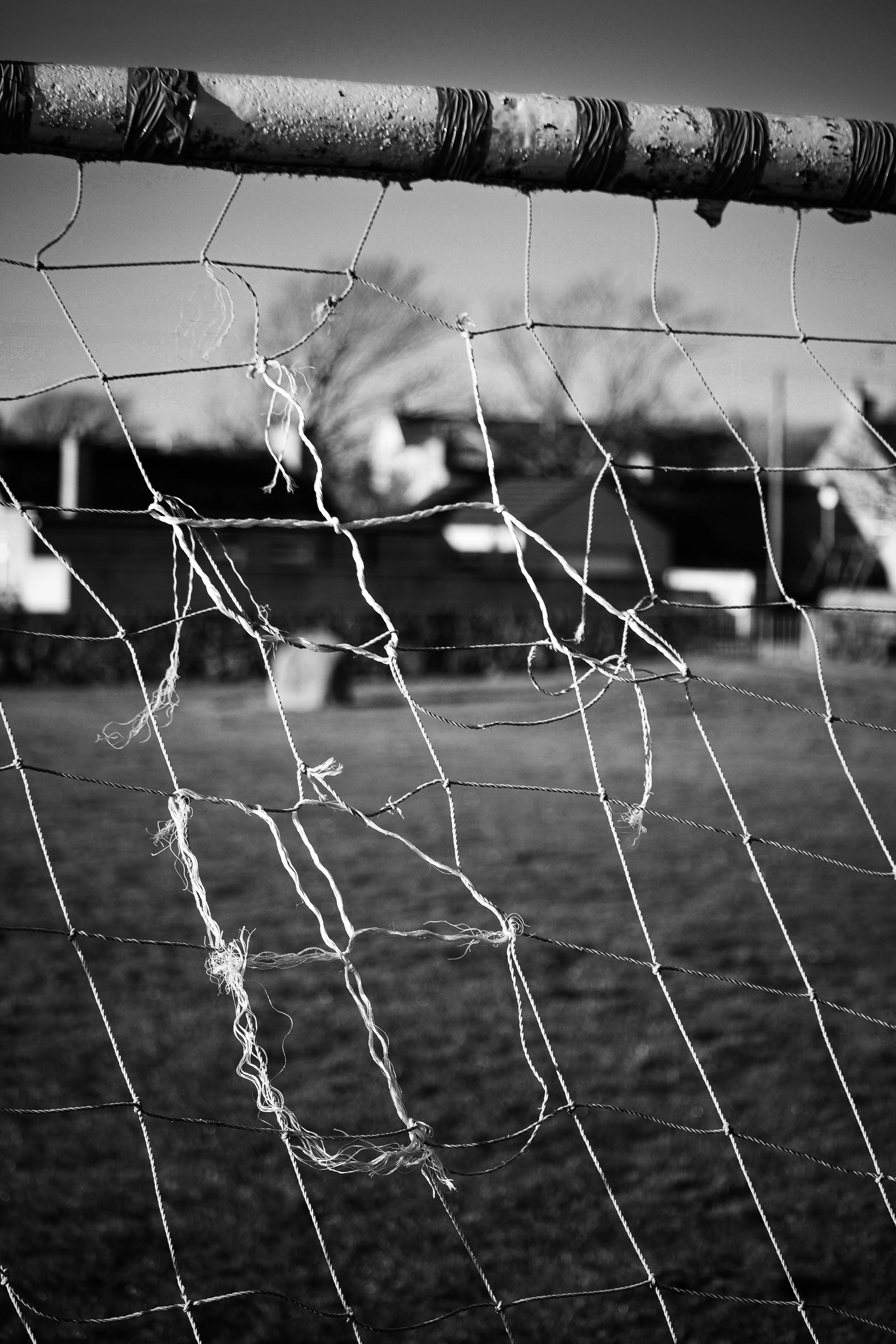 Close-up of a torn soccer goal net with houses and trees in the background.