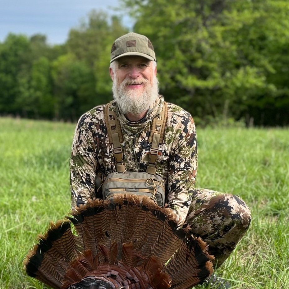 Man in camouflage kneels with a wild turkey in the Arkansas Delta highlighting studioDRIFT's focus on Delta community traditions.
