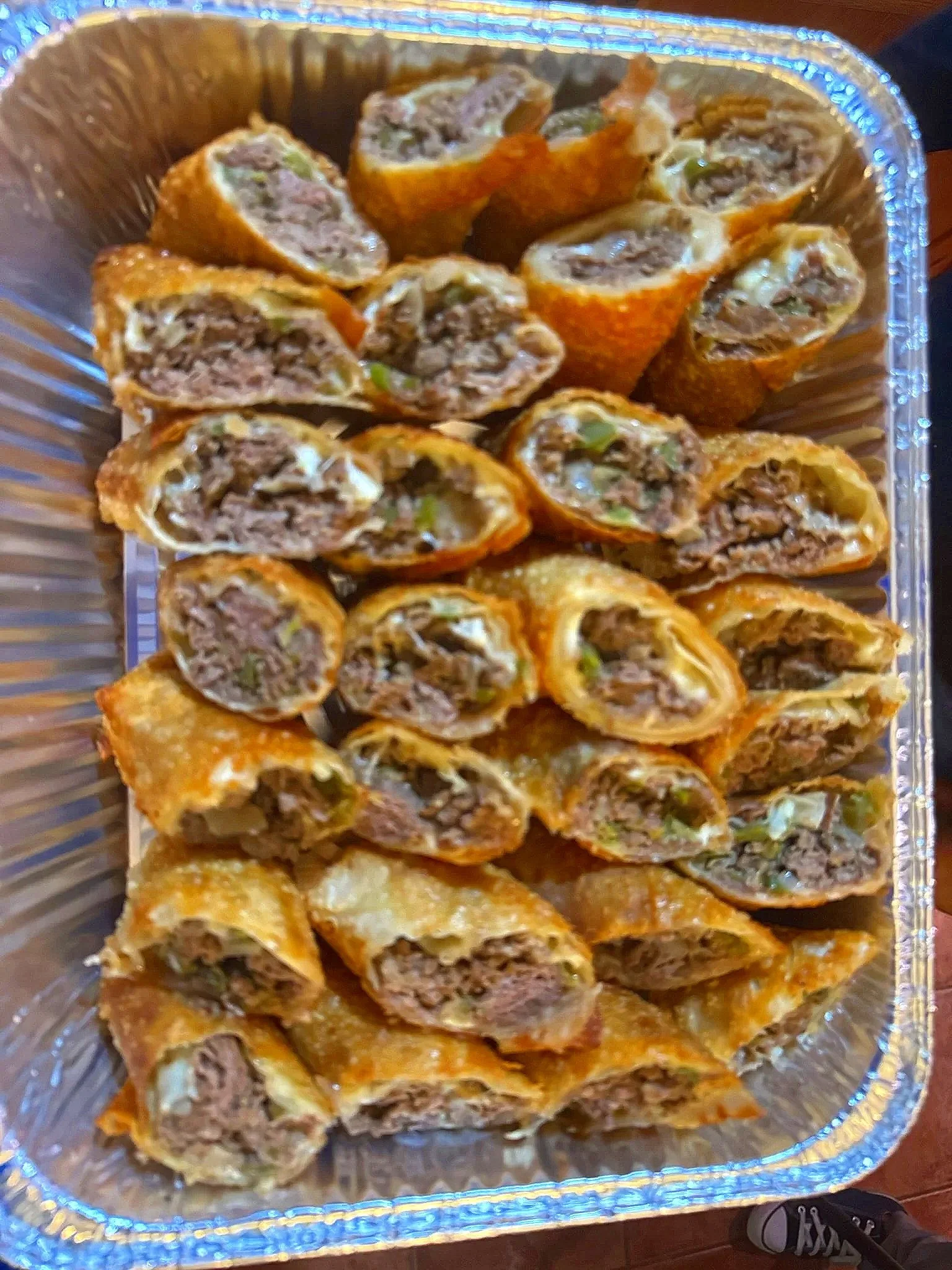 Tray of crispy egg rolls filled with savory beef, vegetables, and seasonings, some cut open showing the filling.