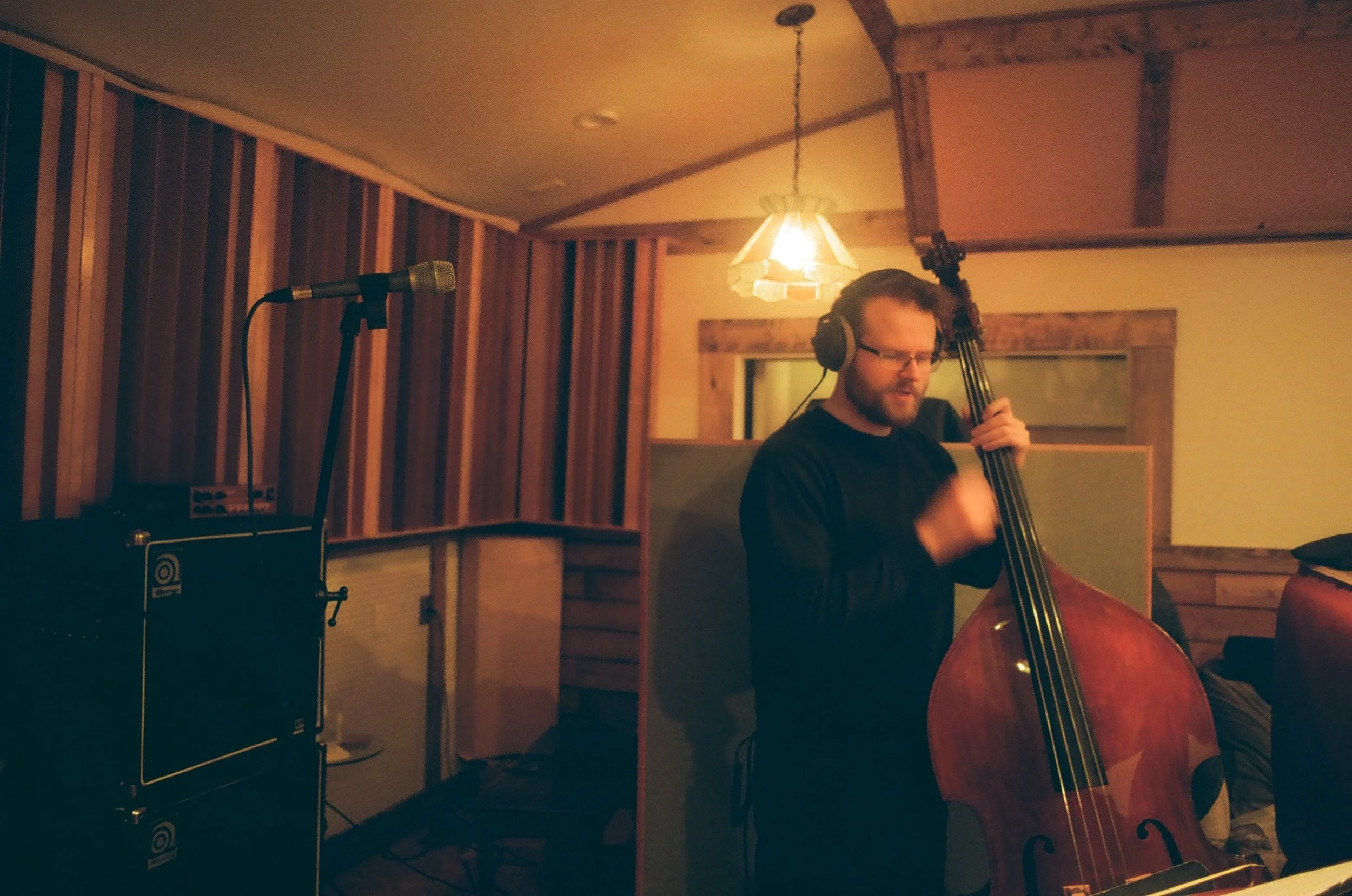 Musician wearing headphones playing a double bass in Holy Cow recording studio with a microphone and amplifier in the background.
