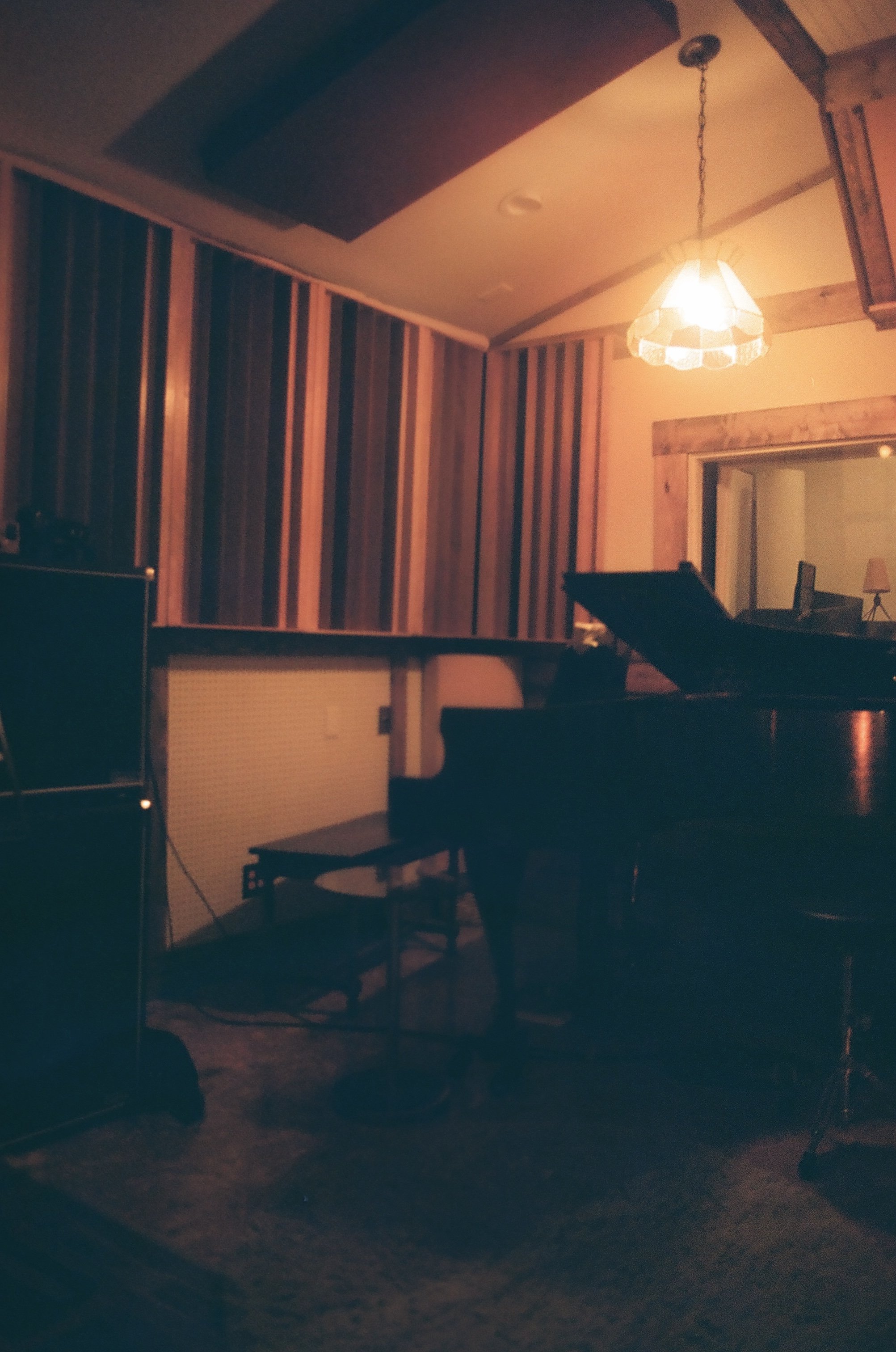 Dimly lit music studio with acoustic panels on the walls, a grand piano, and a hanging light fixture.