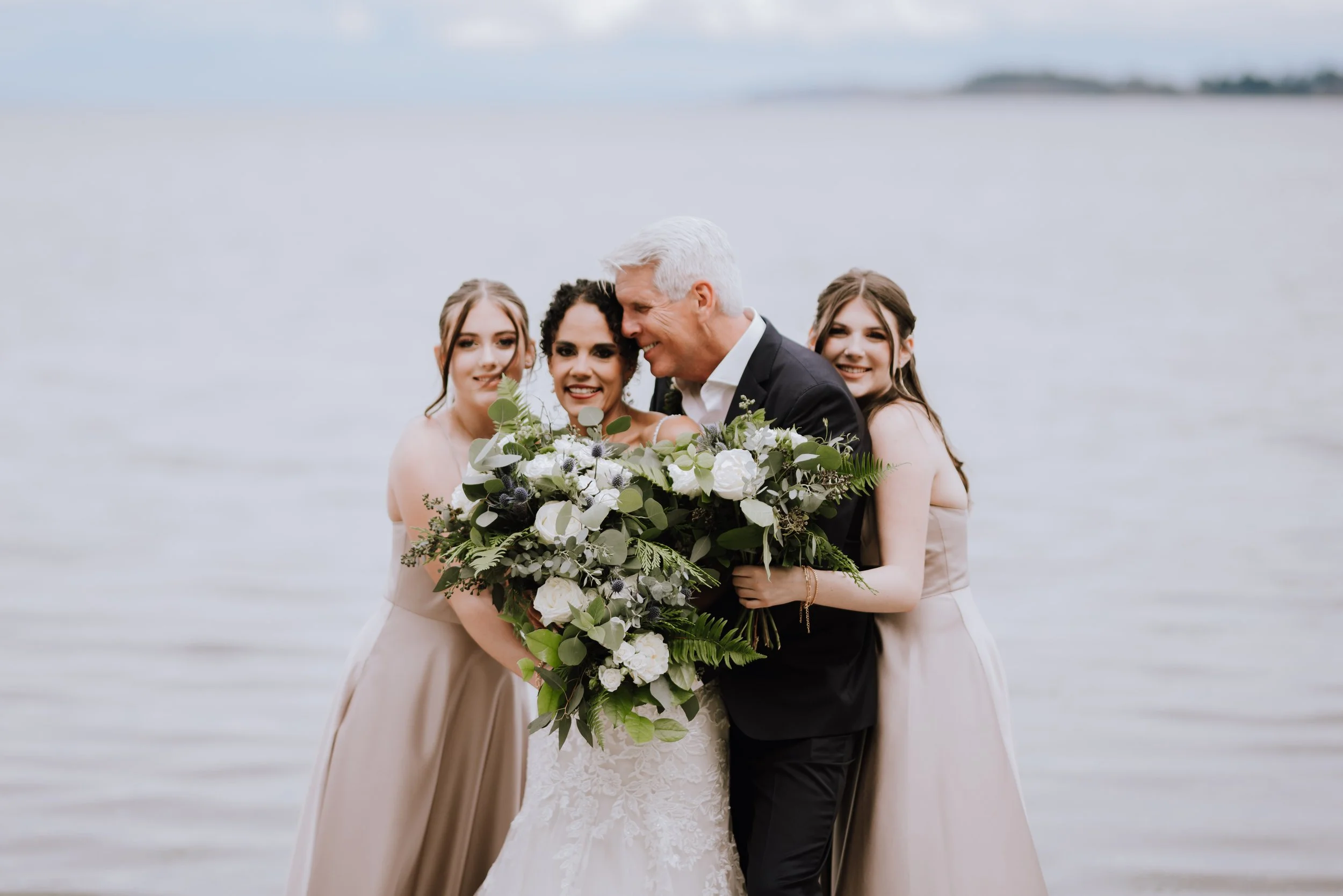 Bride and groom with three bridesmaids standing by a lake, holding a large bouquet of flowers.