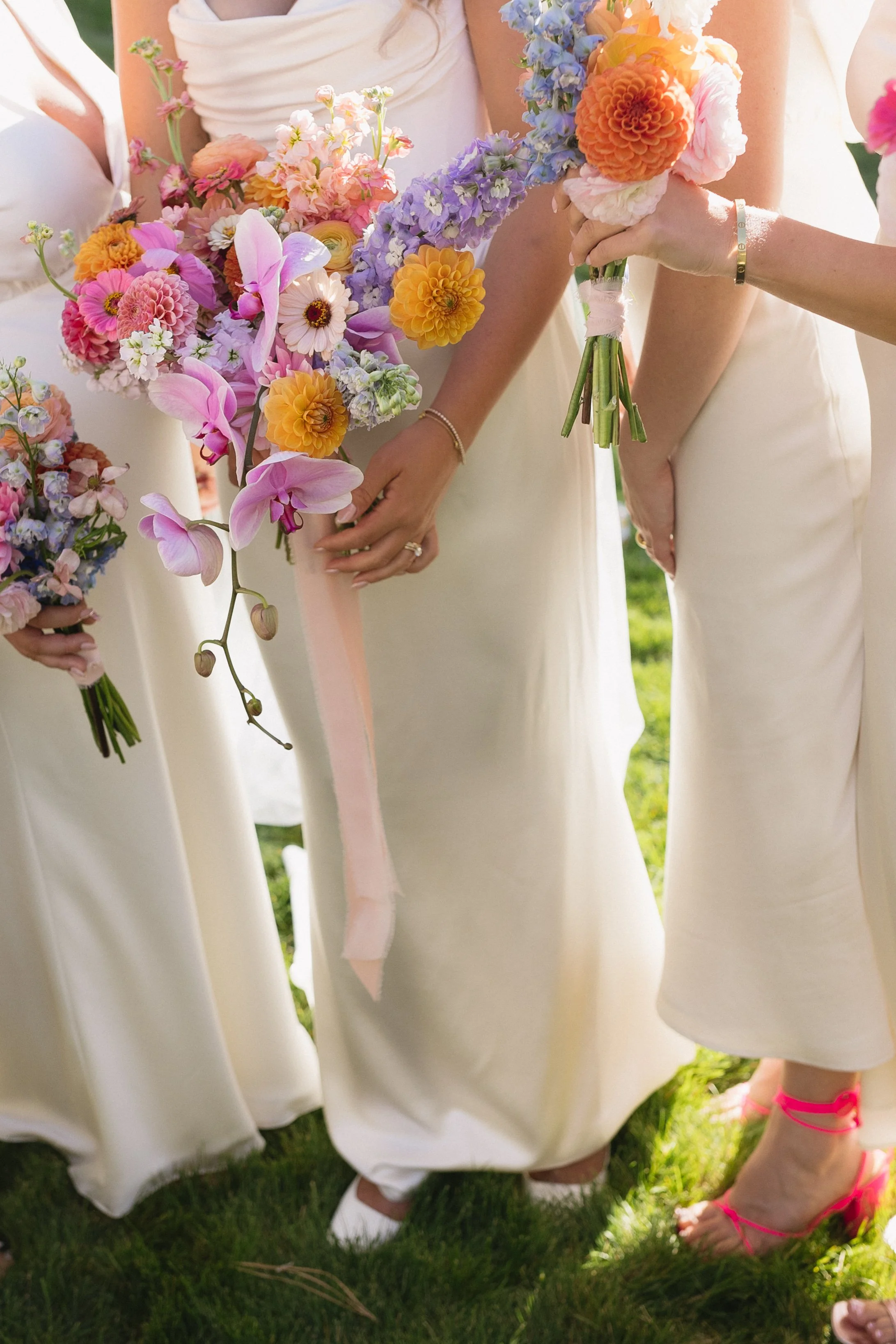 Close-up of a group of women in white dresses holding colorful bouquets of flowers at a wedding ceremony.