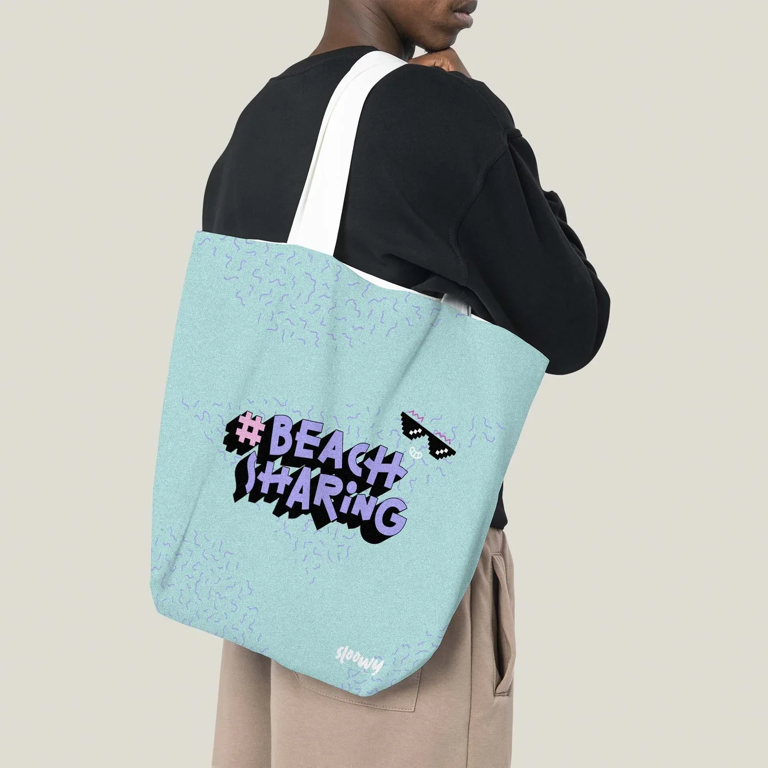 A person carrying a large turquoise tote bag with the hashtag '#BEACHSHARING' and pixelated sunglasses design.