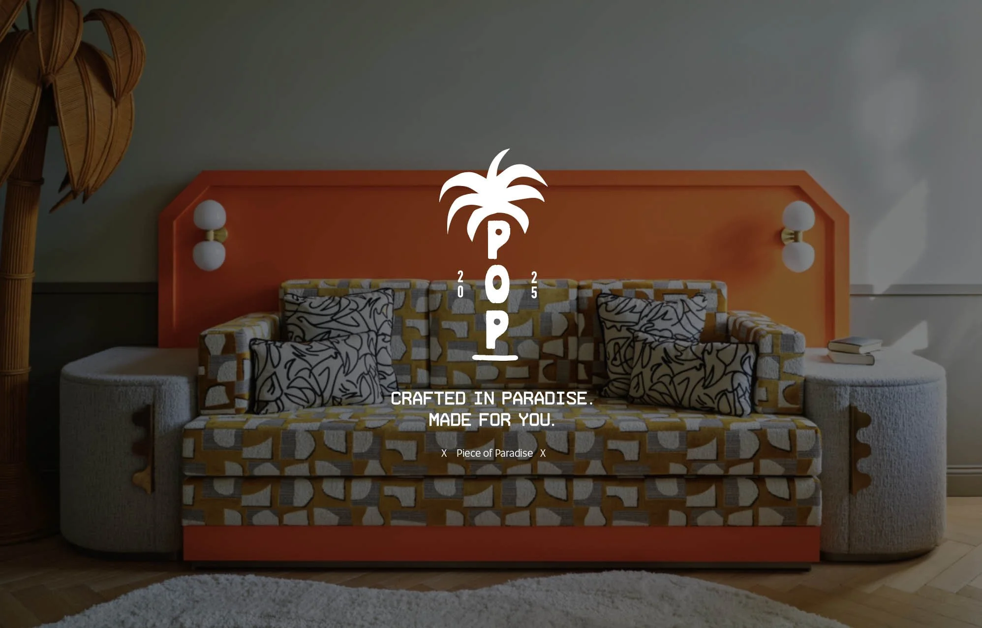 A living room scene with a vibrant orange headboard against a plain wall, flanked by two vintage-style wall sconces with white globes. There is a patterned sofa in front of the headboard, with black and white abstract pillows. To the left, part of a bamboo or wicker lamp is visible, and there is a small stack of books on the right side of the sofa. A white shaggy rug is on the wooden floor in the foreground.