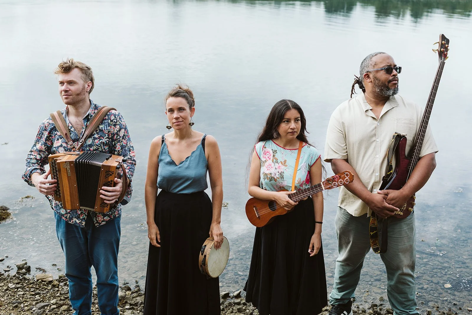Quatre personnes debout au bord d'un lac, deux hommes et deux femmes, chacun tenant un instrument de musique, attendent ou posent.