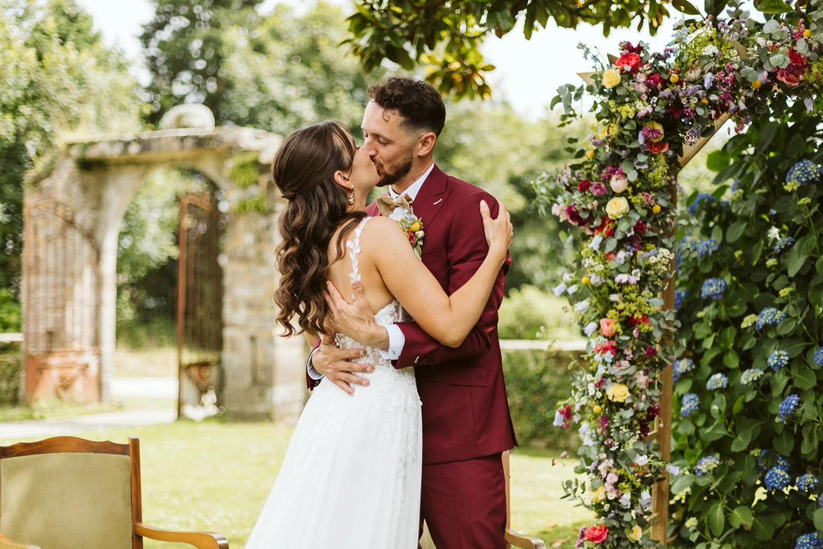 Un couple de mariés s'embrassant sous un arc de fleurs lors d'un mariage en extérieur.