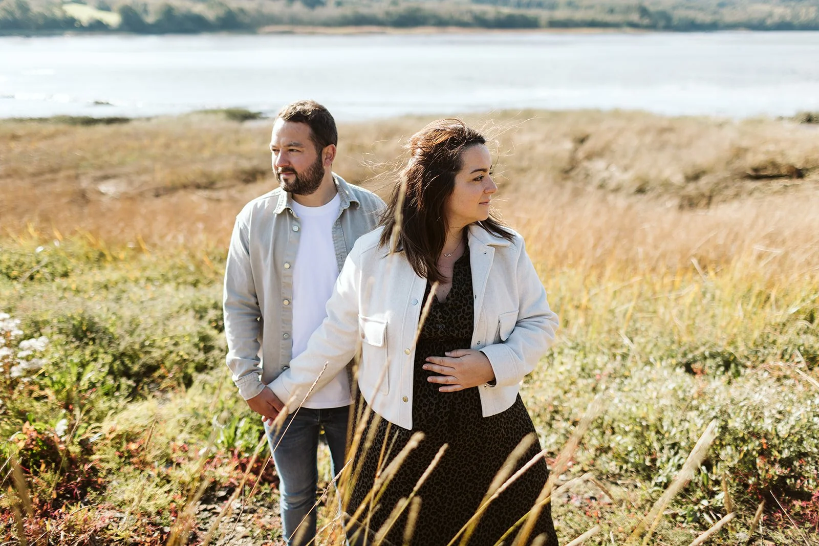 Un homme et une femme se tenant par la main dans un champ près de l'eau, en plein air, par une journée ensoleillée.