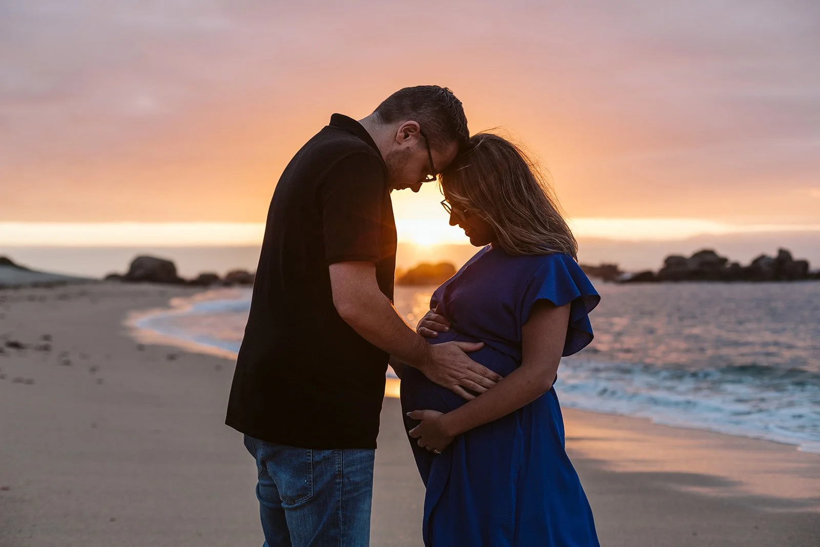 Un couple regardant la femme enceinte, à la plage au coucher du soleil.