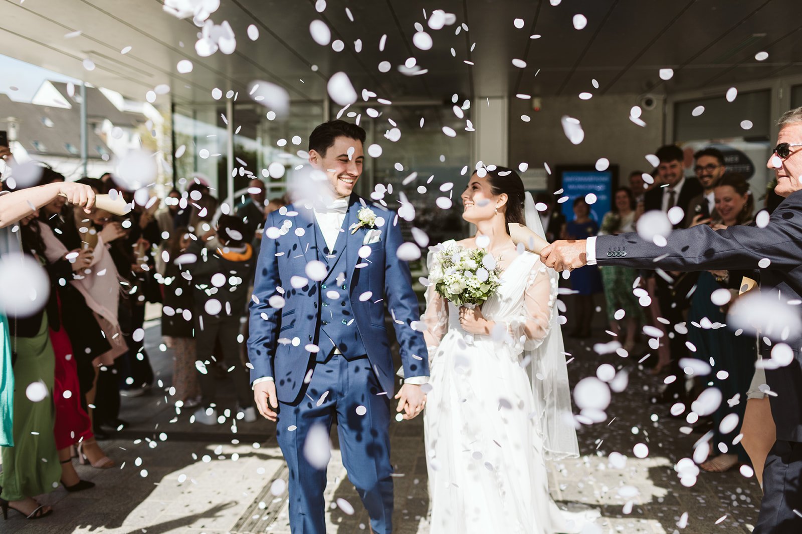 Le couple marié sourit tandis que les invités jettent des confettis blancs lors de leur mariage en plein air.