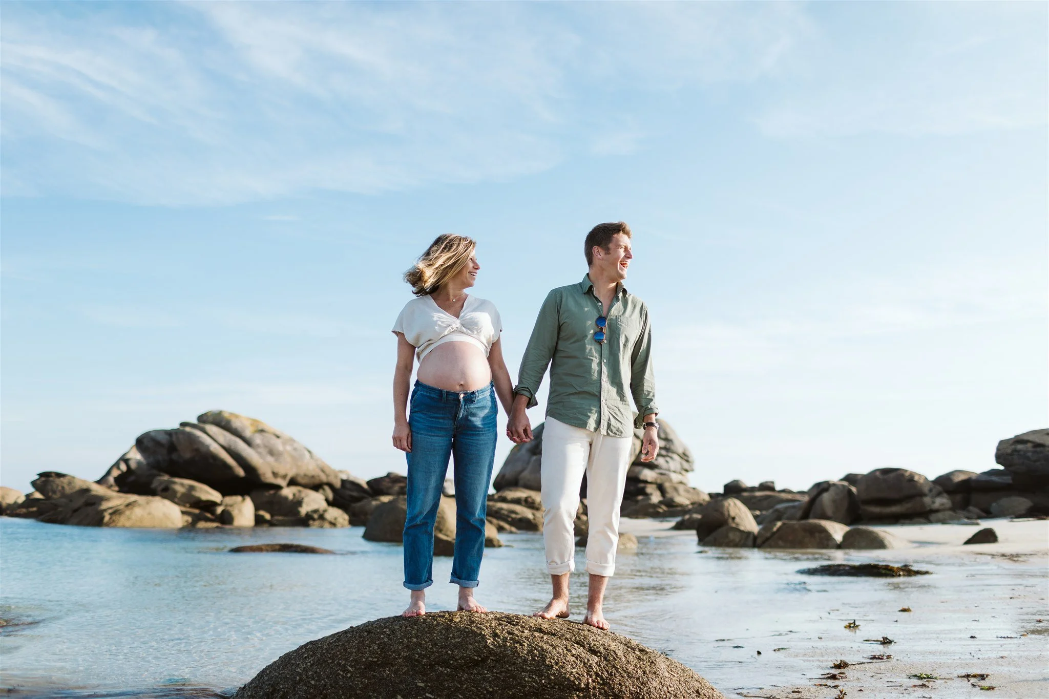 Un couple se tient main dans la main sur une roche à la plage par une journée ensoleillée.