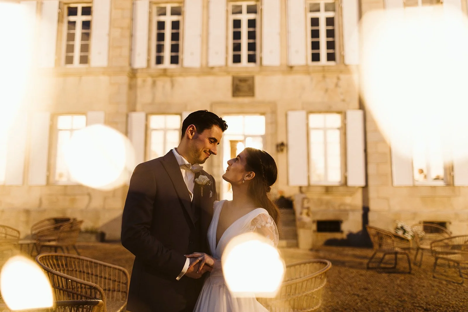 Un couple de mariés se regarde tendrement devant un bâtiment illuminé la nuit, lors de leur mariage.
