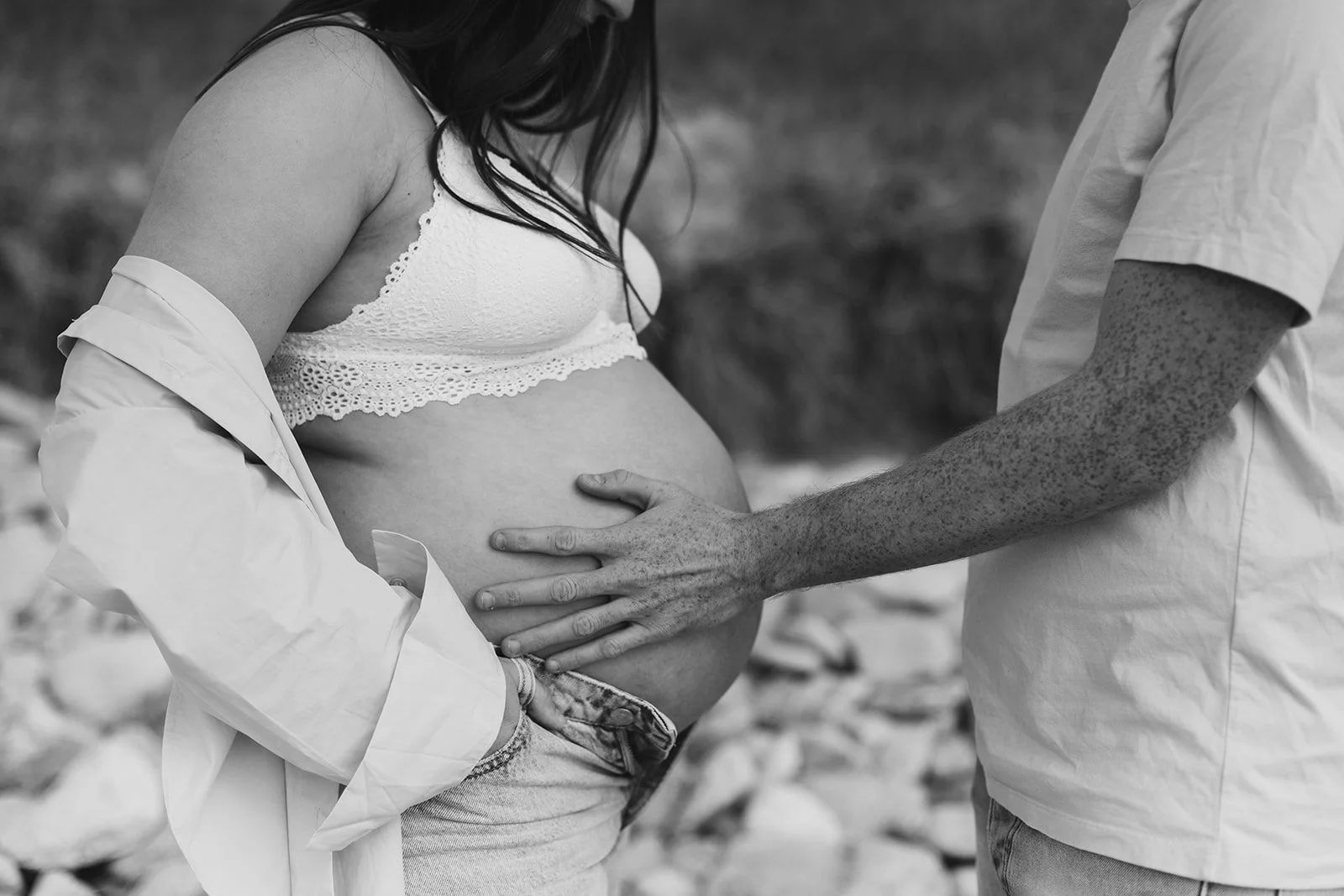 Une femme enceinte et un homme se touchant le ventre dans un cadre naturel, en noir et blanc.
