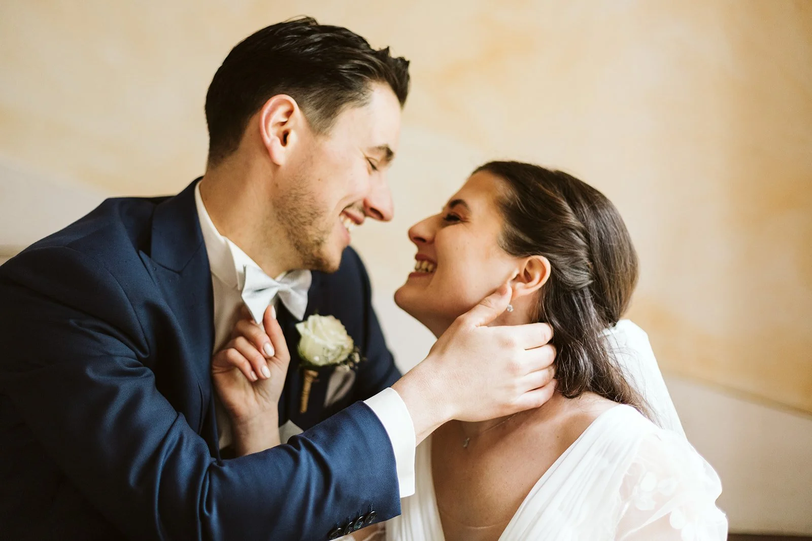 Un couple de mariage souriant et se regardant tendrement, l'homme en costume bleu et la femme en robe blanche.