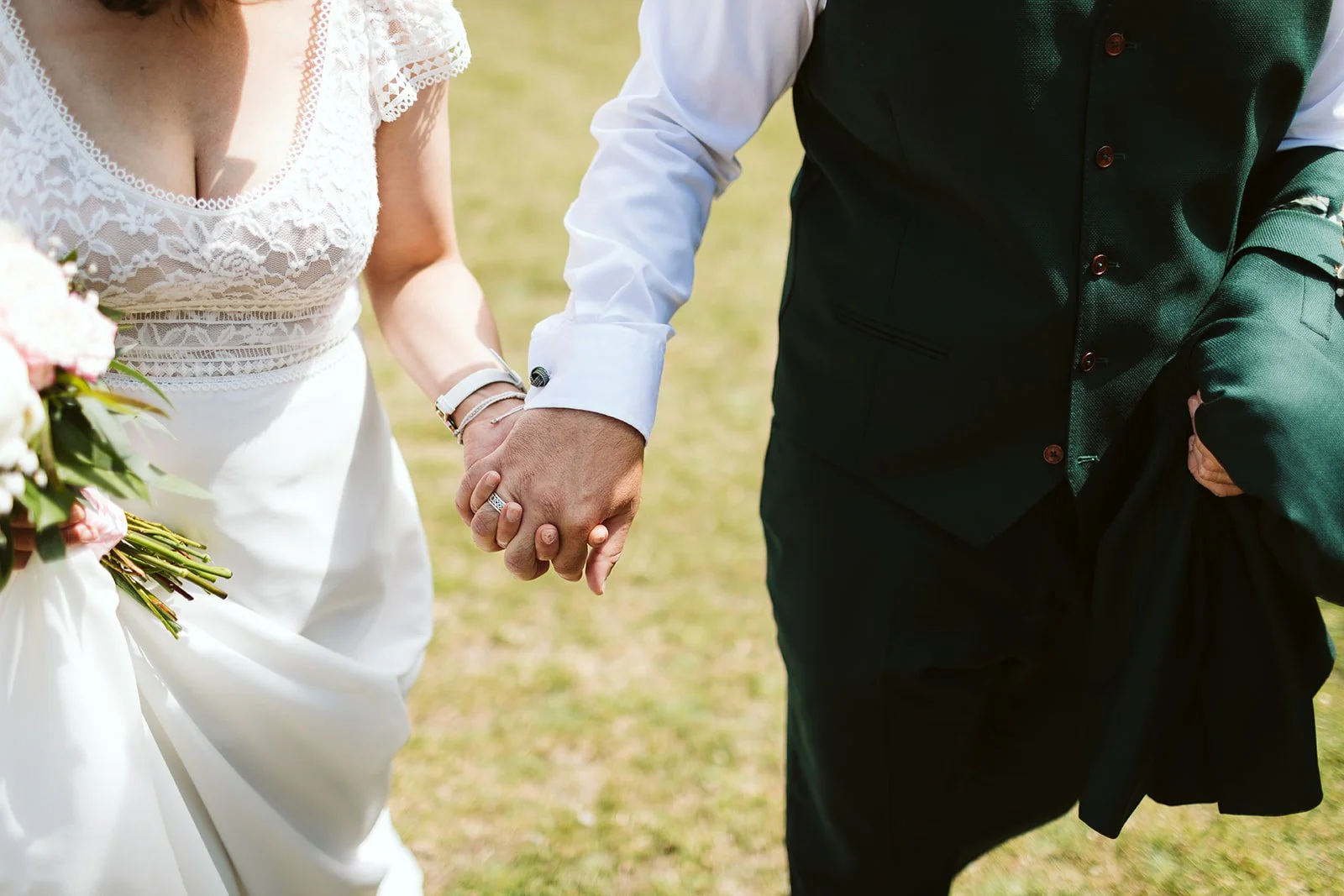 Un couple de mariés tenant la main lors de leur mariage en plein air.