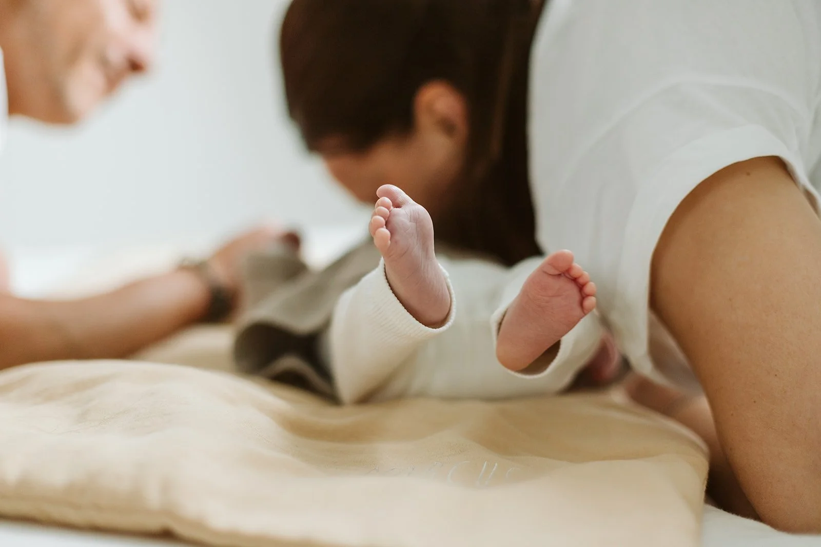 Un bébé en couche faisant du tummy time avec deux adultes à proximité.