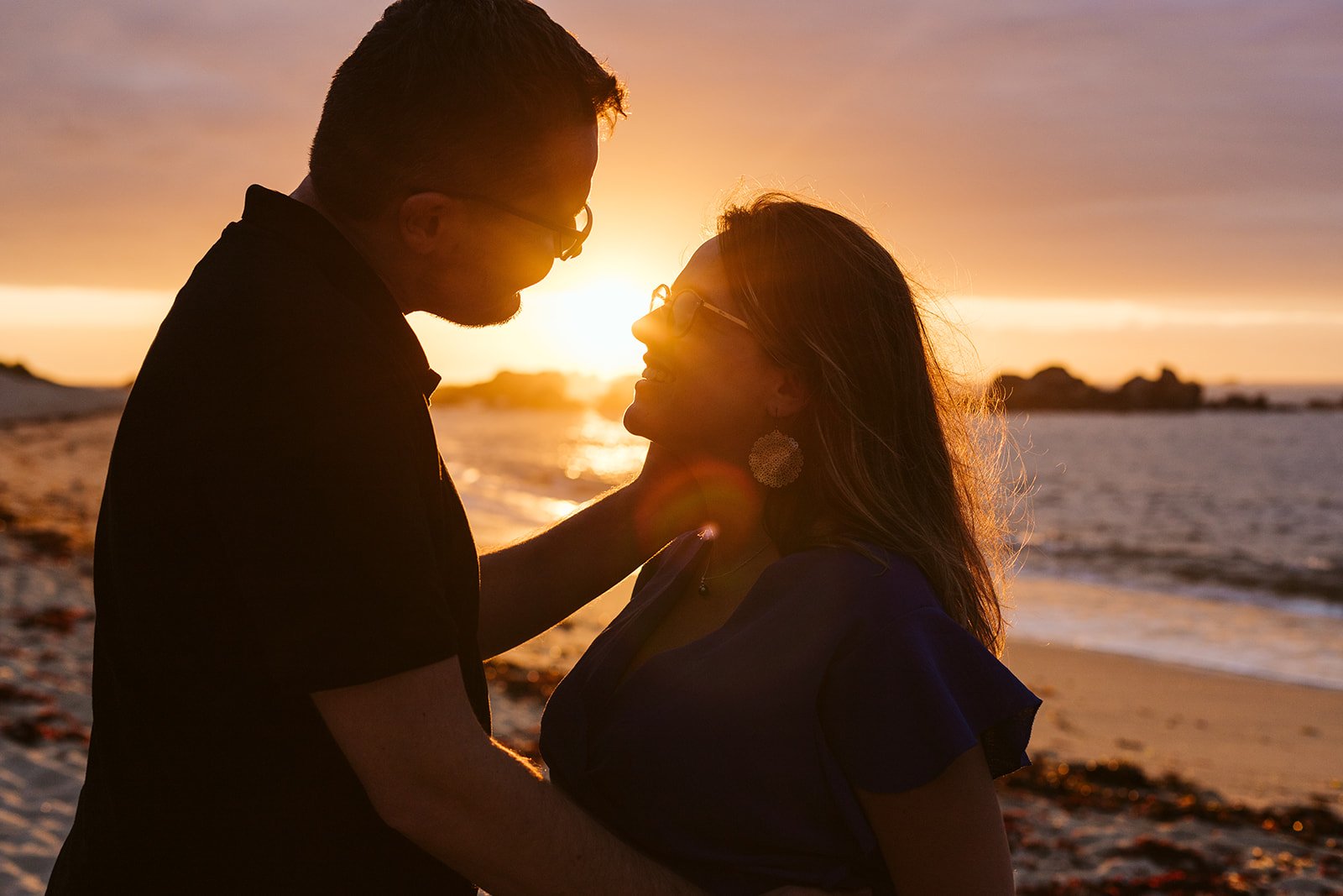 Un couple silhouette face à face sur la plage au coucher du soleil, partageant un moment tendre.