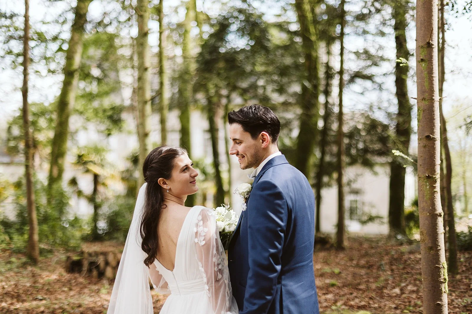 Un couple de mariés dans une forêt, regardant l'un l'autre, souriants, lors de leur mariage.