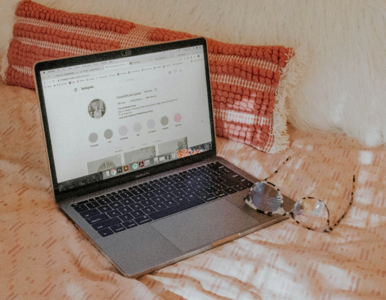 Laptop on a bed with Instagram profile open — promoting From Invisible to In-Demand live mini-course by Good + Well Consulting, a small business visibility training.