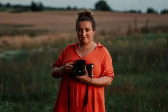Foto von Lisa Lange, Dokumentarische Familienfotografin aus Angermünde mit rotem Kleid und Kamera in der Hand.